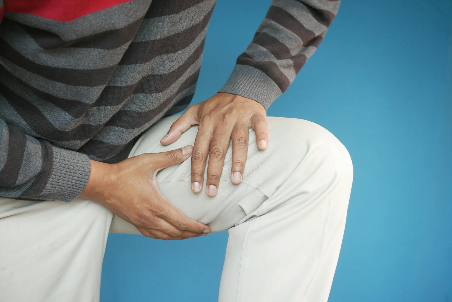 Close-up of a man's hands on his knee, showing pain or injury, on a blue background. - knee pain relief exercises