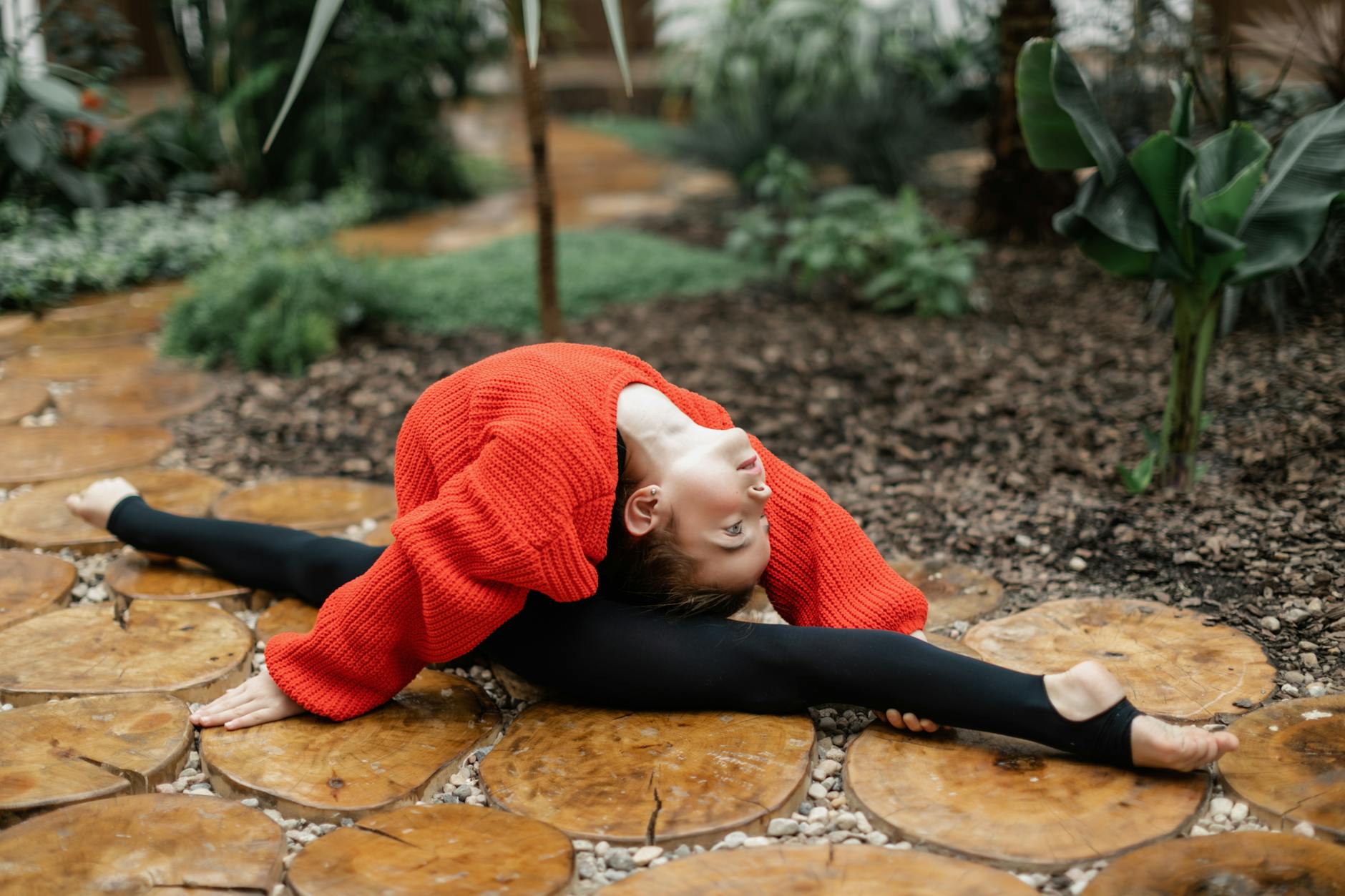 A young girl stretches in a split on a wooden path, showcasing remarkable flexibility in a garden. - leg flexibility exercises