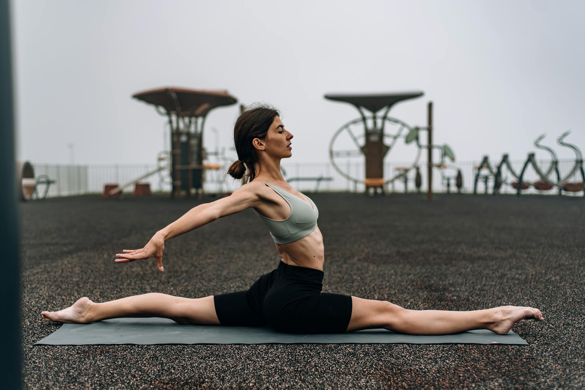 A woman performing yoga splits on a mat outdoors, promoting fitness and flexibility. - lower body flexibility
