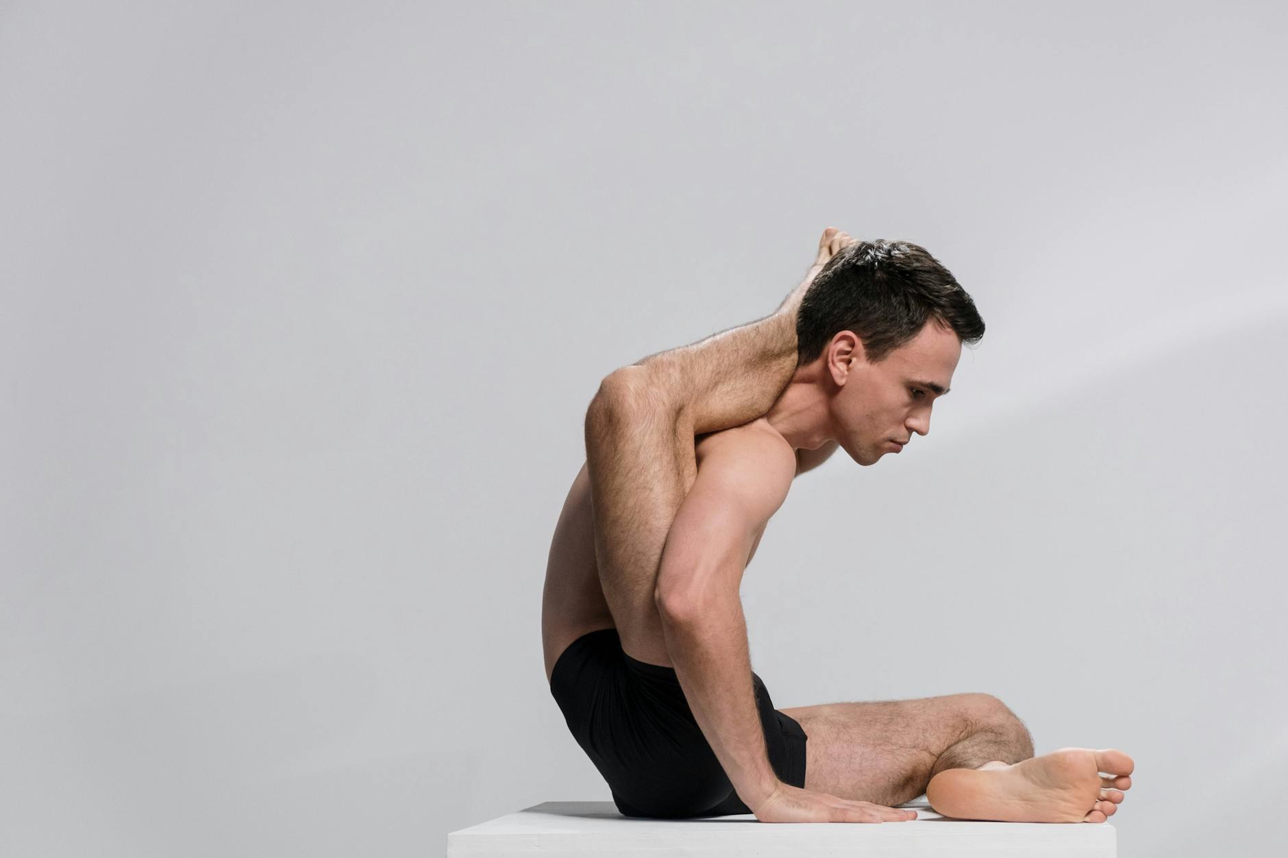 A man demonstrating an advanced yoga pose indoors, showcasing flexibility and concentration. - lower body flexibility