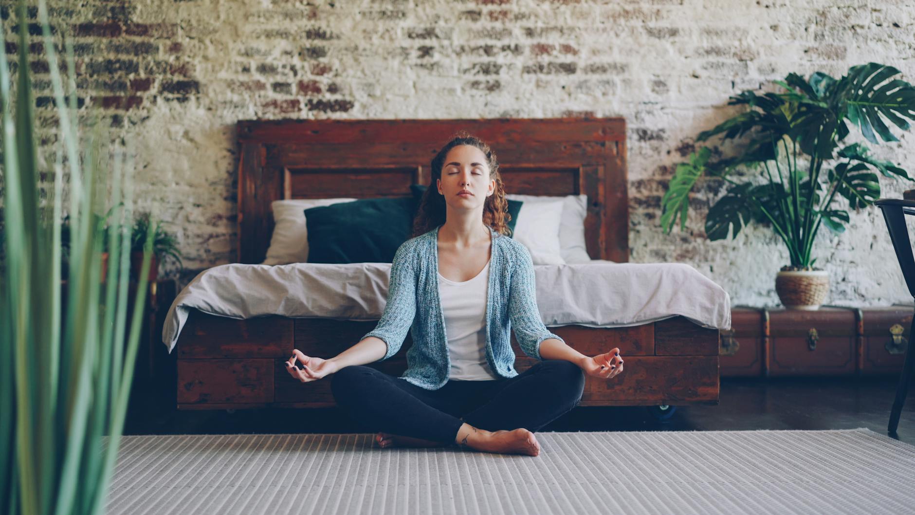 Tranquil scene of a woman meditating in a stylish bedroom with natural decor. - mental clarity tips
