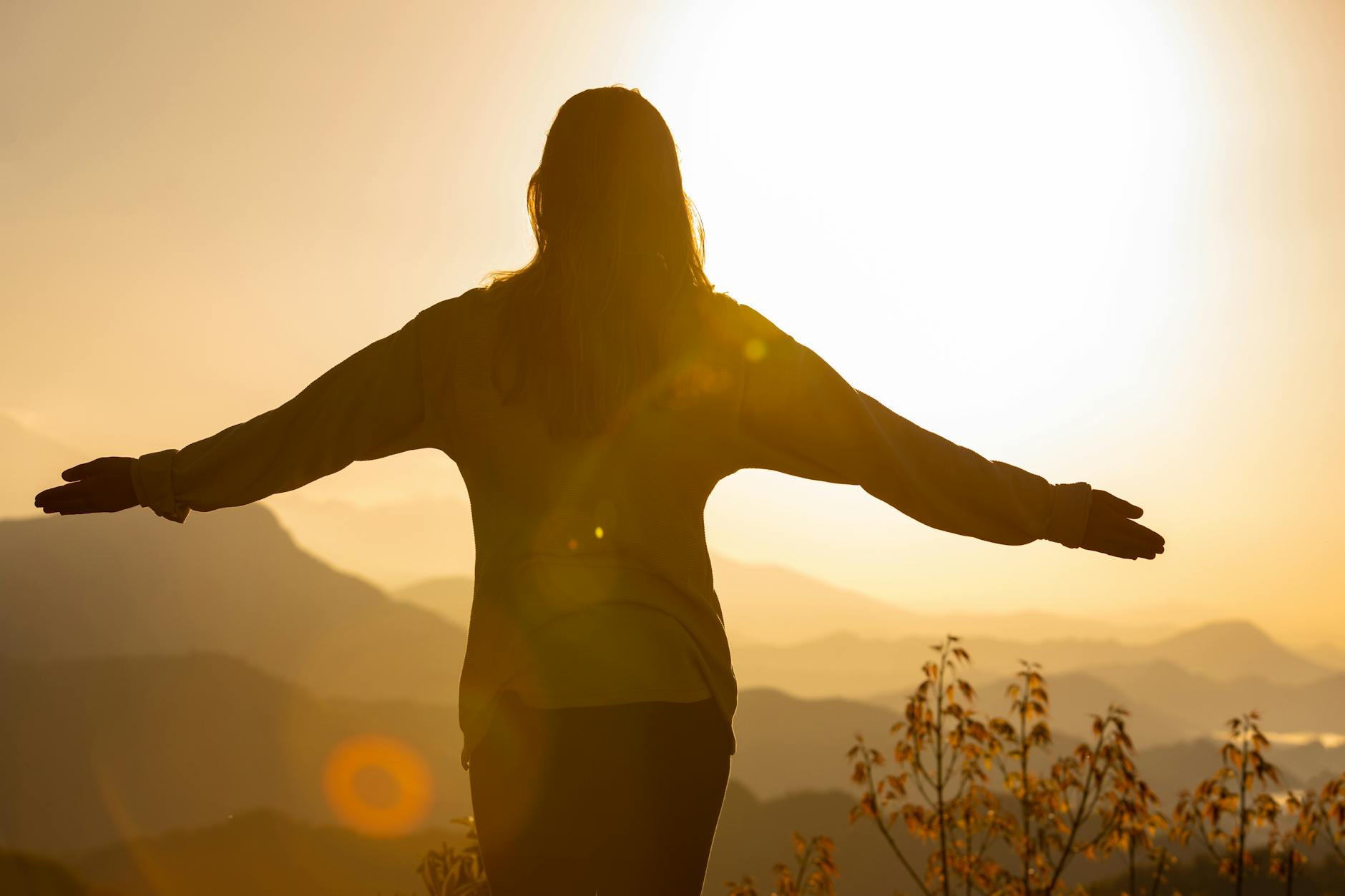 A woman stands with arms open, embracing the sunrise in a mountainous landscape, creating a tranquil silhouette. - mindfulness for fresh start