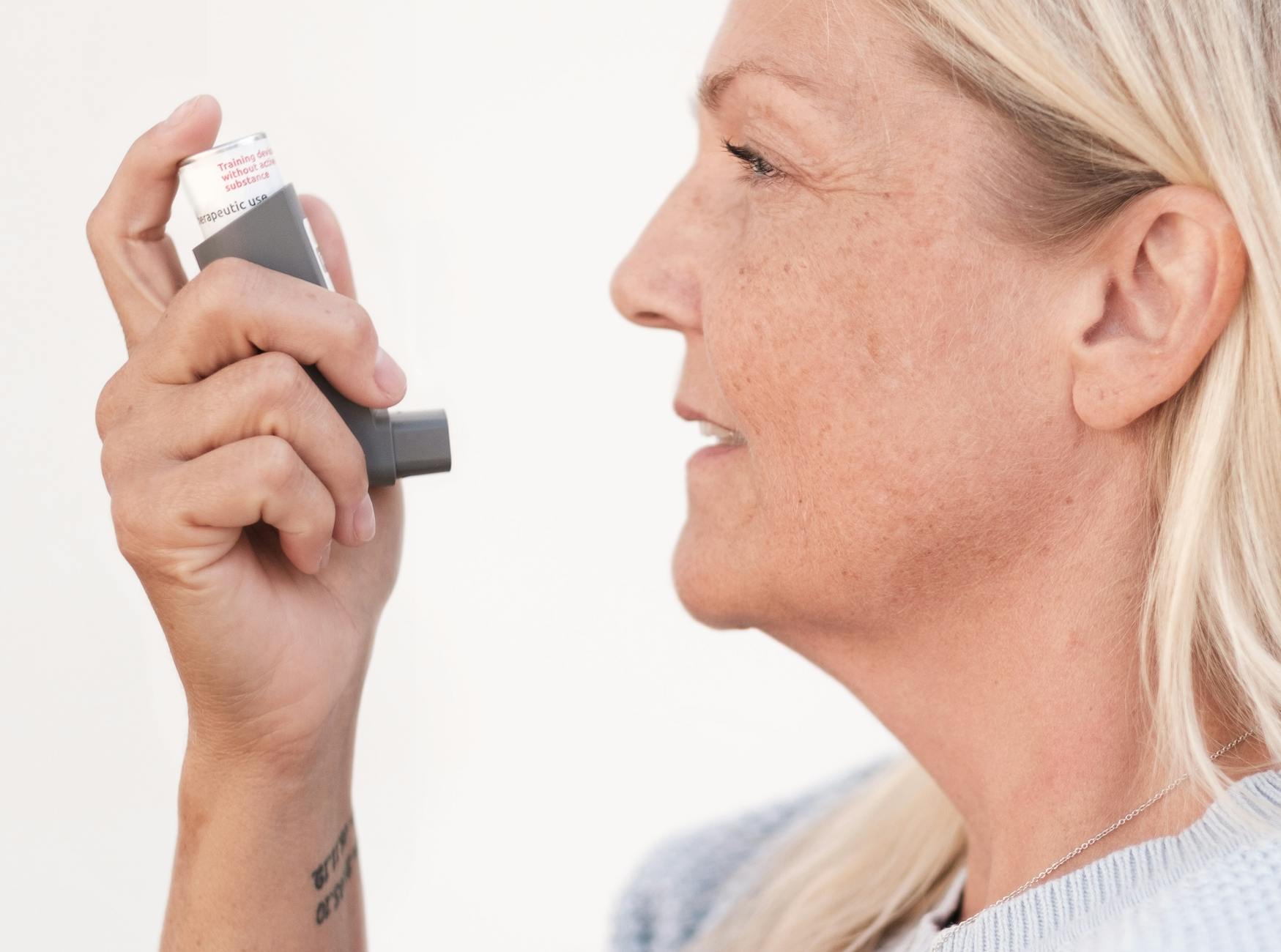 Middle-aged woman using an asthma inhaler to alleviate breathing difficulties. - natural allergy relief