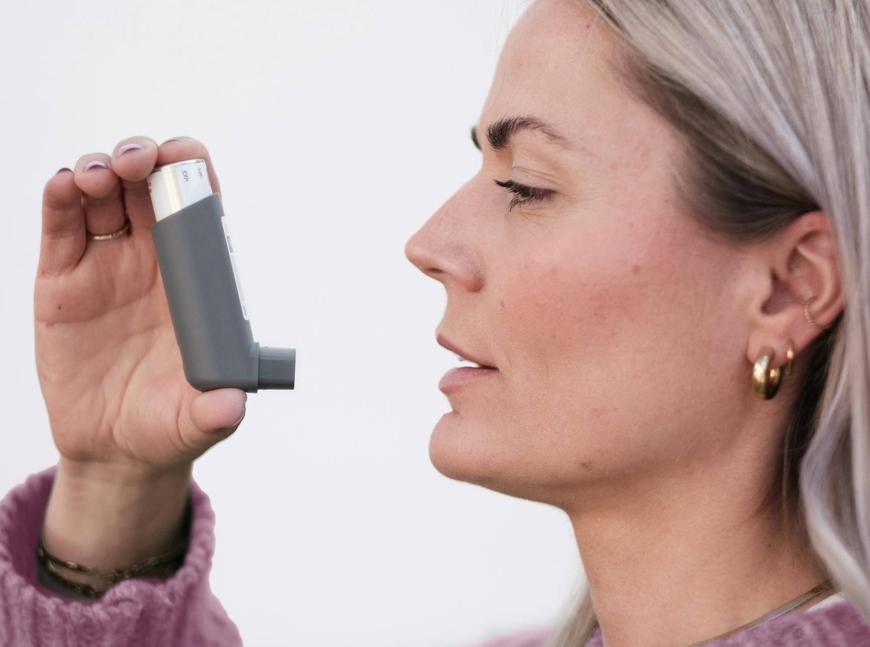 Close-up of a woman using an asthma inhaler, isolated on a white background. - natural allergy relief