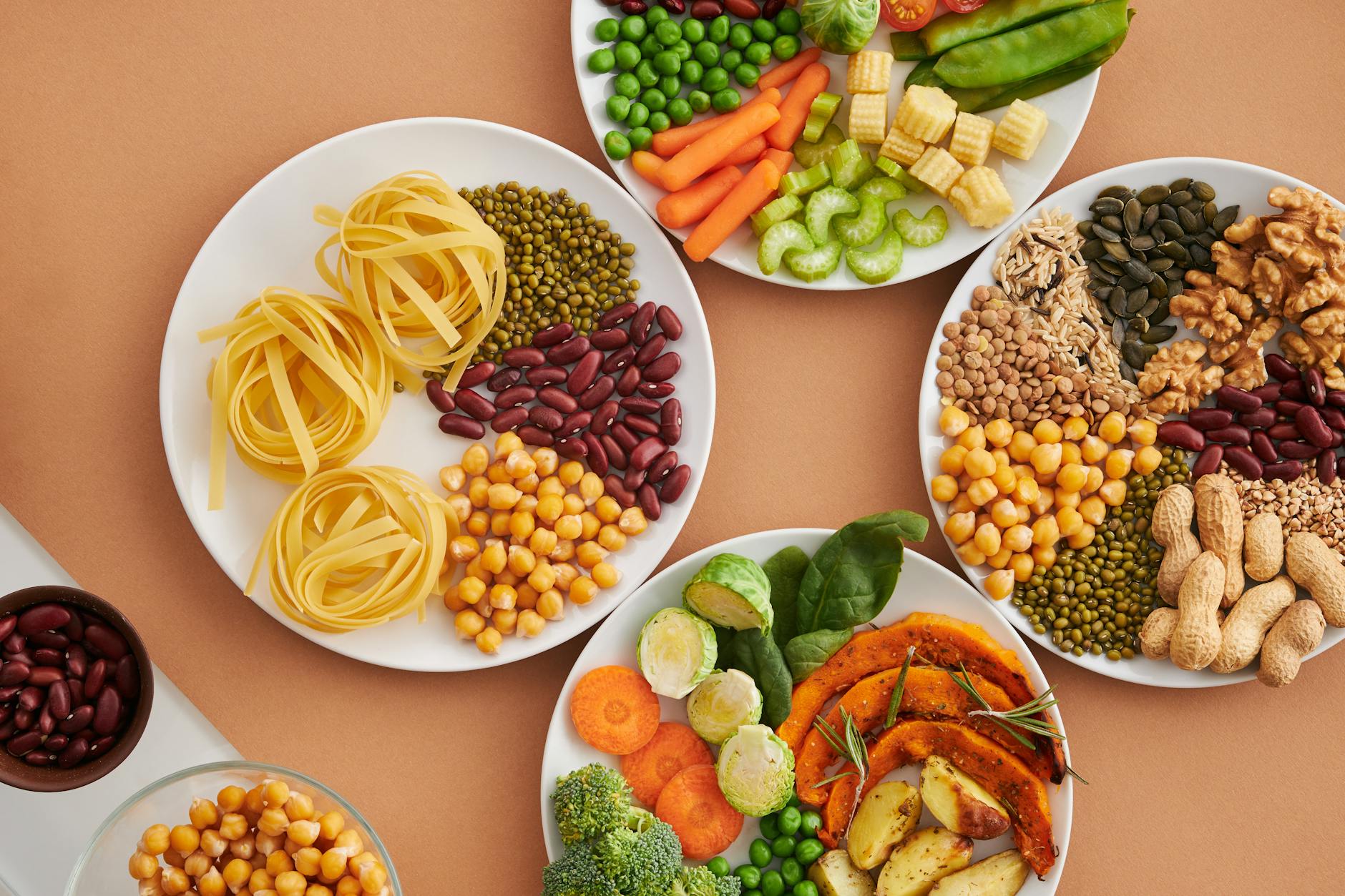 A vibrant mix of legumes, vegetables, nuts, and pasta arranged on white plates showcasing a balanced, healthy diet. - organic plant protein
