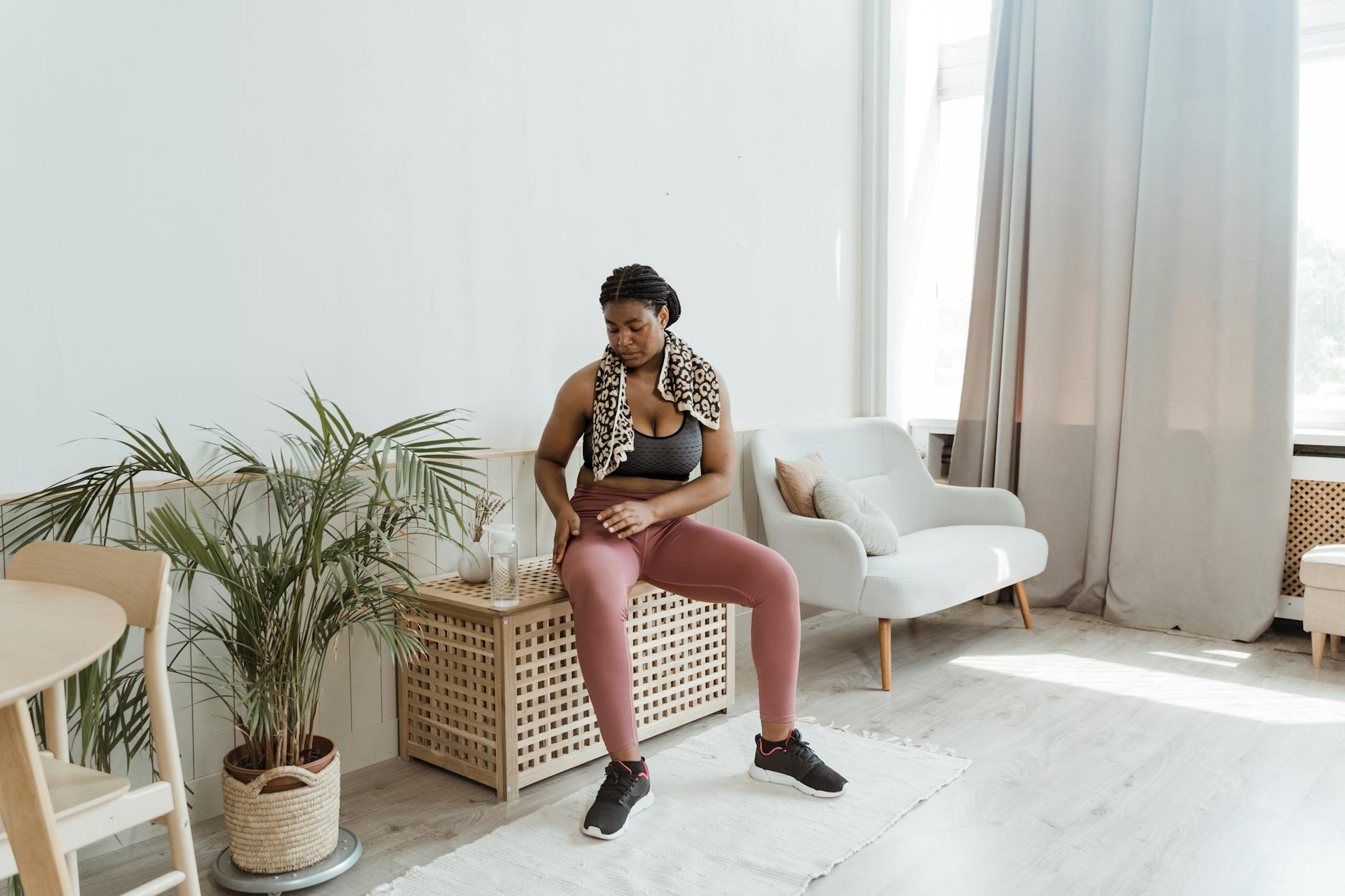 Black woman in activewear resting at home after exercise, sitting on a chair with a towel around her neck. - post winter workout