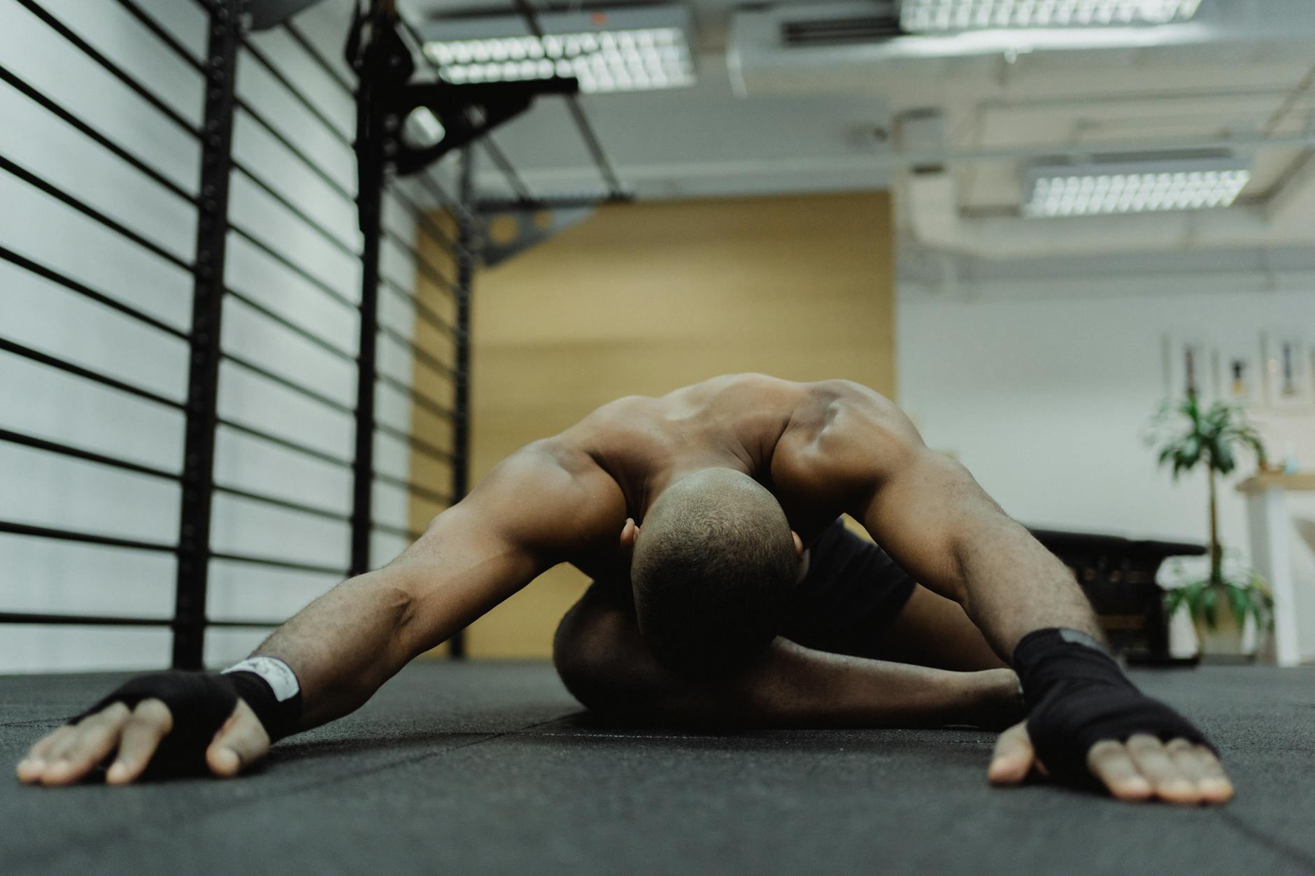 Shirtless man performing stretching exercise on gym floor, focusing on flexibility and strength. - posture exercises gym