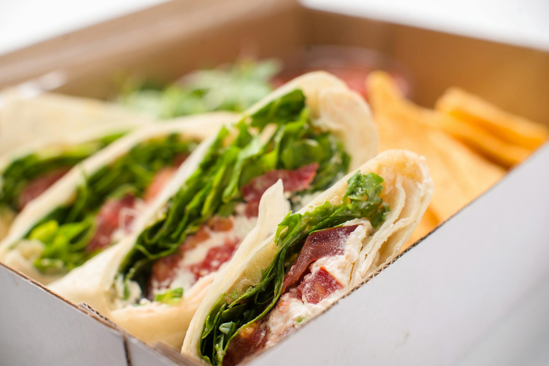 Delicious wrap sandwich featuring greens, bacon, and cheese in a take-out box. - quick lunch recipes
