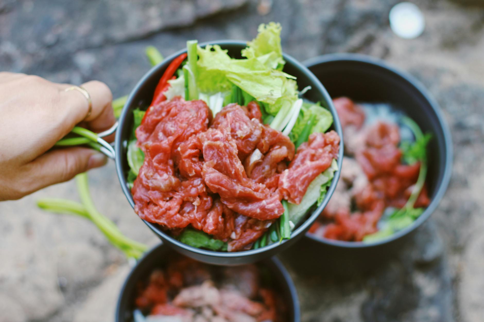 From above of crop unrecognizable person showing small pan with fresh green salad and sliced raw beef - raw food nutrition
