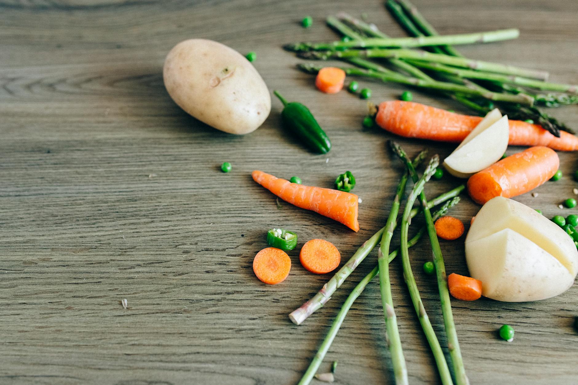A variety of fresh organic vegetables including carrots, peas, and asparagus on a wooden surface. - seasonal produce spring