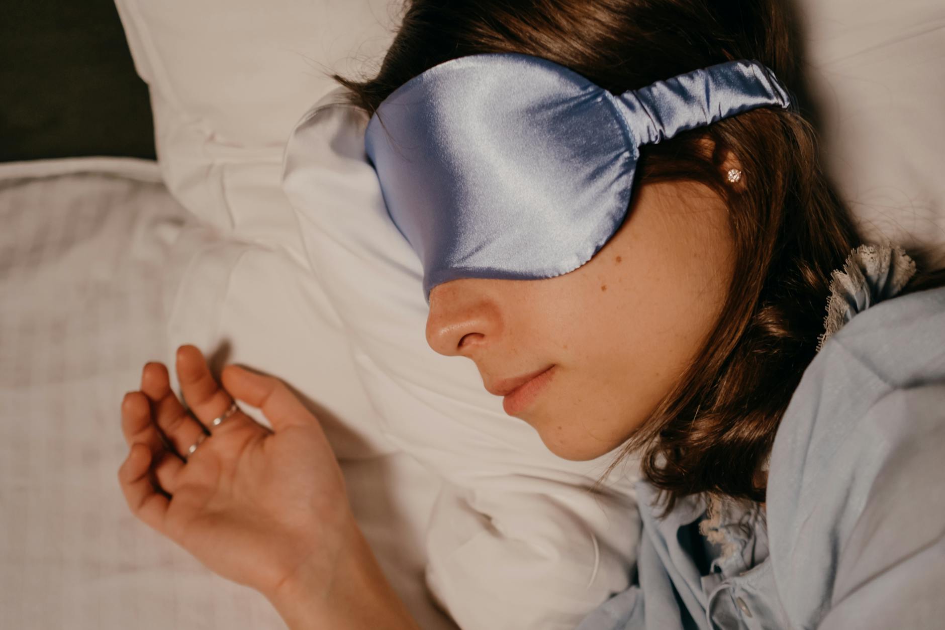 A woman wearing a silk eye mask sleeping peacefully on a pillow. - sleep deprivation causes