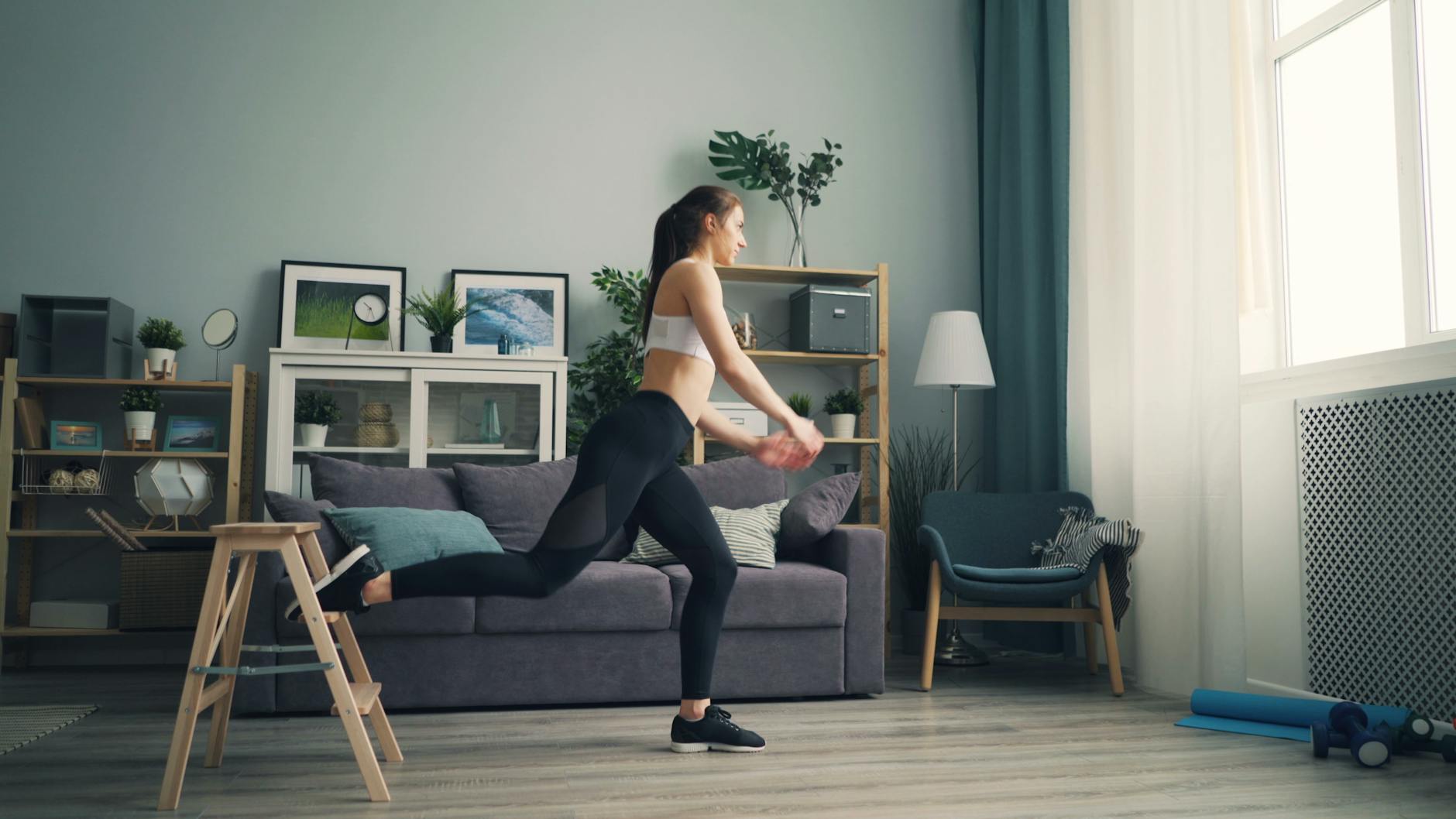A woman in sportswear working out indoors using a chair for support, demonstrating leg exercises. - small space workouts