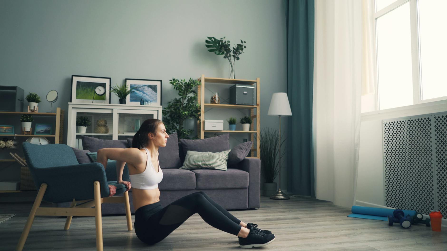 Woman doing tricep dips at home using a chair for support, promoting fitness indoors. - small space workouts