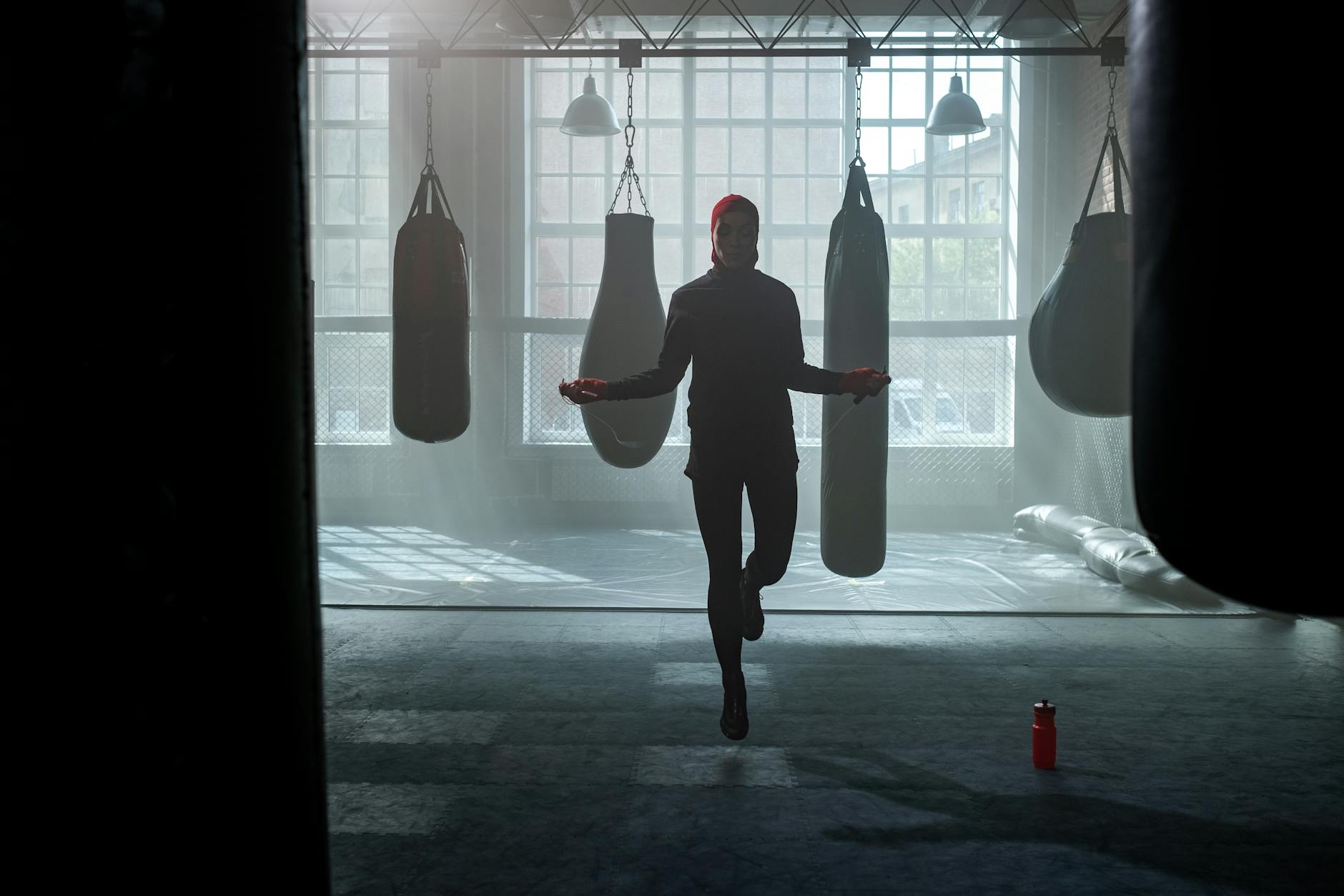 A woman exercises by jumping rope in a gym filled with punching bags. - spring cardio fat burn