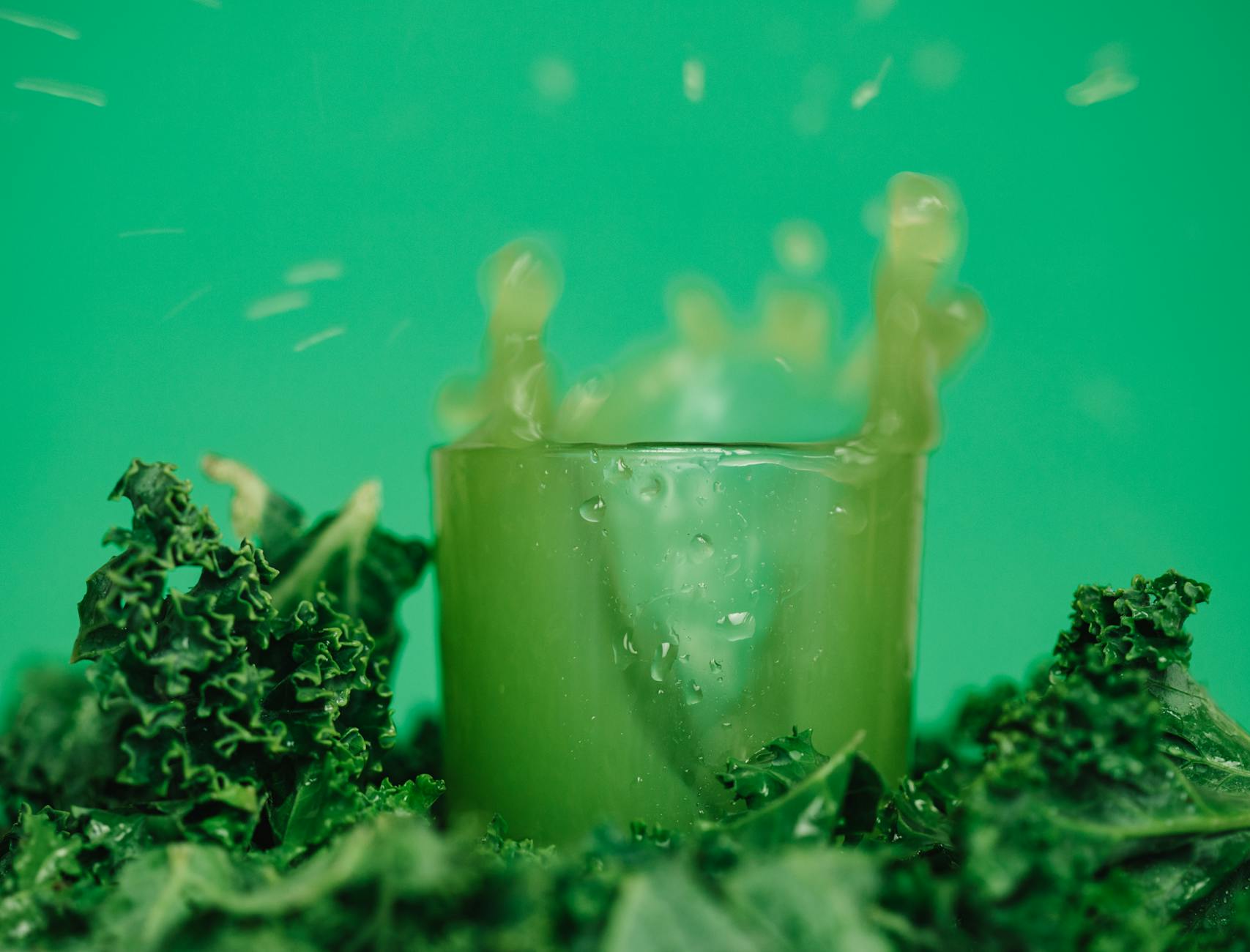 Transparent glass with drops on surface full of delicious colorful fresh detox green juice splashing in air near curly lettuce leaves - spring energy foods