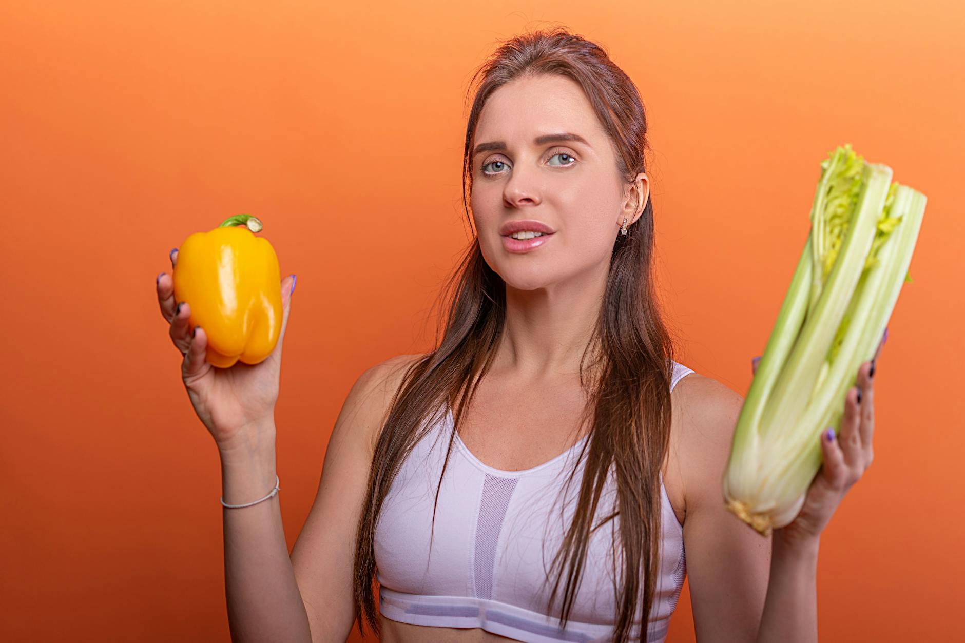 Woman holding yellow bell pepper and celery, showcasing healthy eating. - spring energy foods