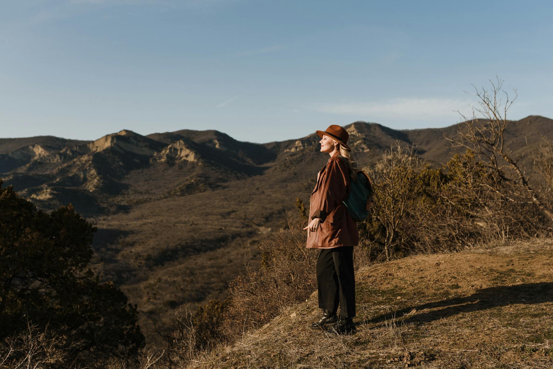A woman in a hat stands on a mountainside, enjoying a scenic landscape view. - spring hiking for beginners