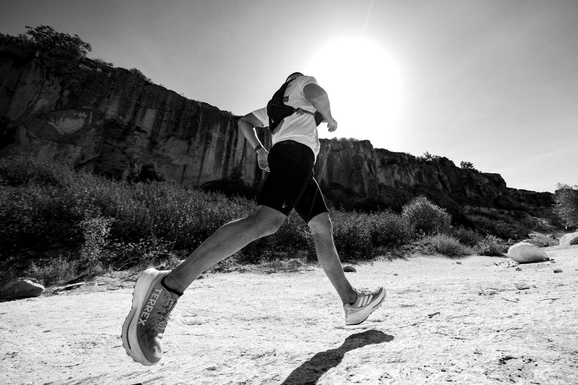 Black and white photo of a trail runner beneath a sunny cliff, showcasing movement and determination. - spring hiking running