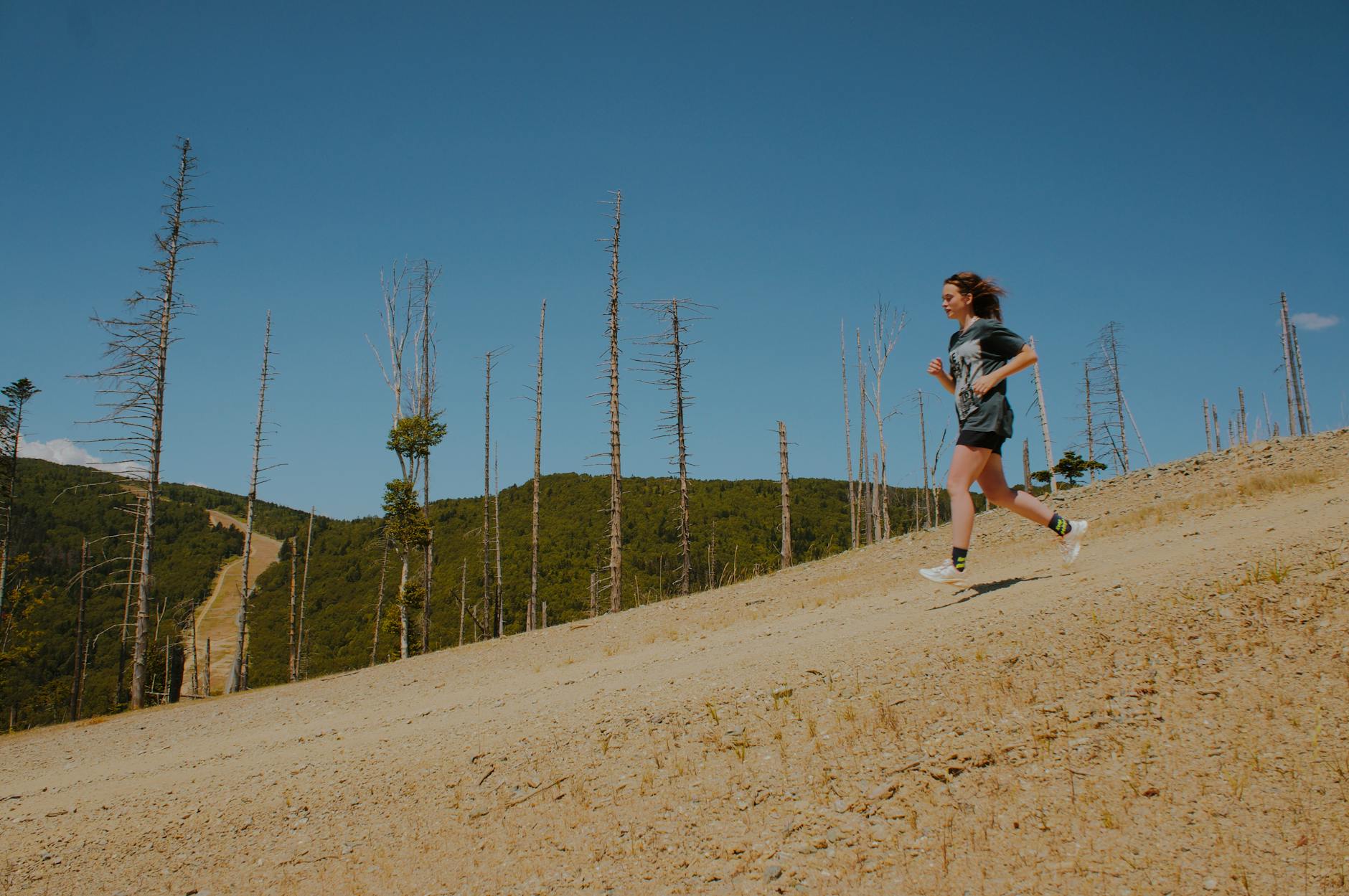 A lone woman enjoys a summer run on a scenic hillside path surrounded by nature and clear blue skies. - spring hiking running
