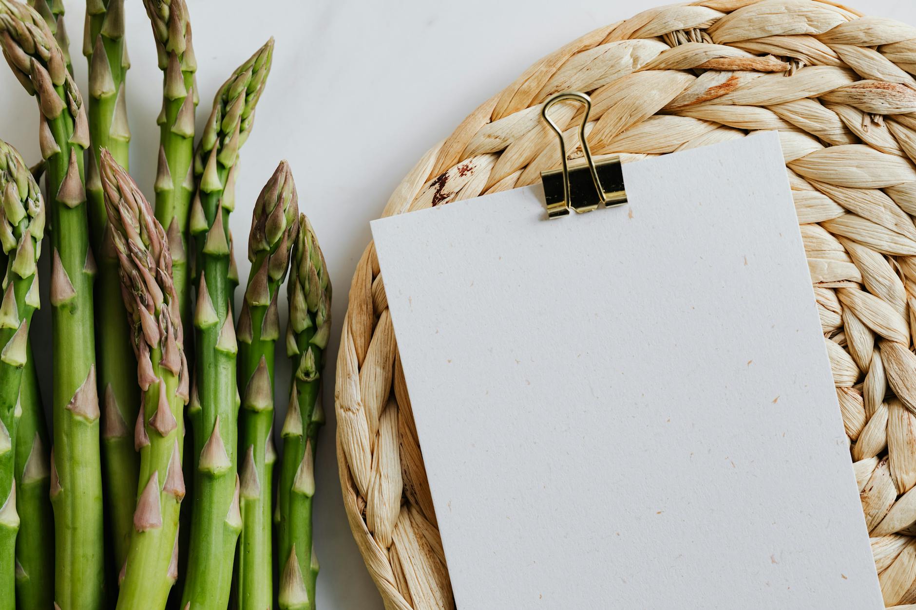 Top view of paper fastened by paper clip with asparagus pods on white table - spring nutrition macros