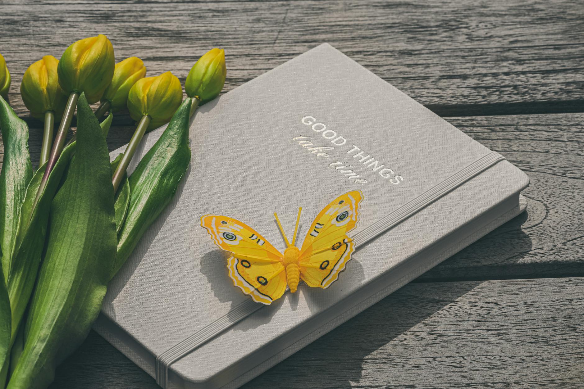 A yellow butterfly rests on a notebook with tulips, capturing a serene and inspirational moment. - spring reset journal prompts