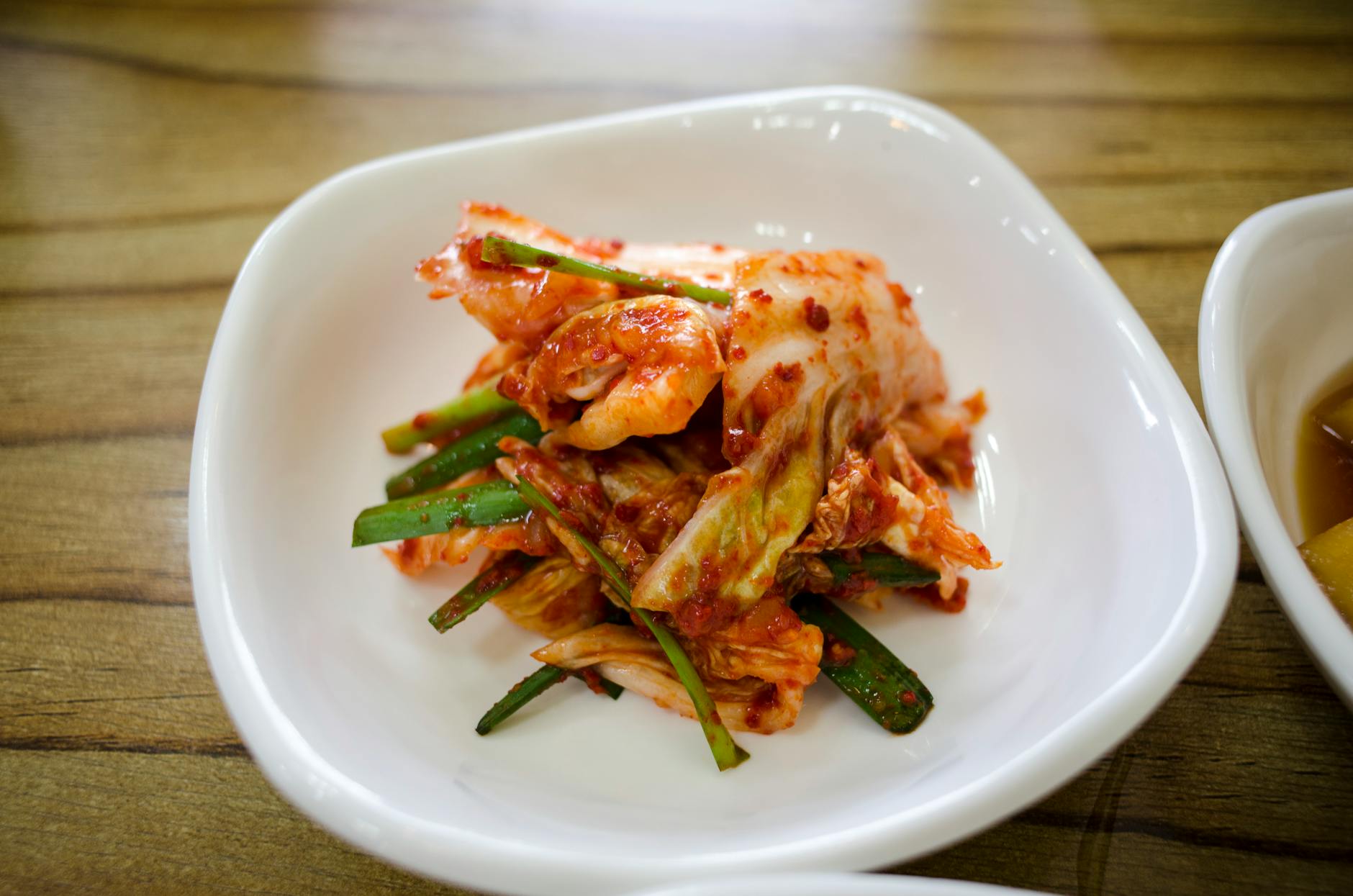 Close-up of traditional Korean kimchi served in a white ceramic dish on a wooden table. - benefits of fermented foods