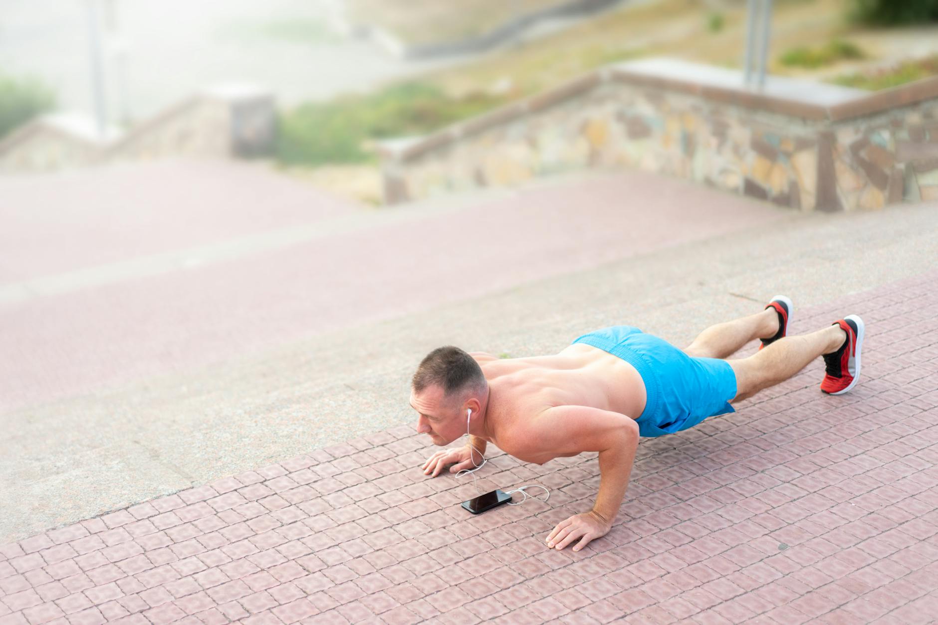 A fit man listening to music and doing push-ups outside on stairs. - daily workout plan