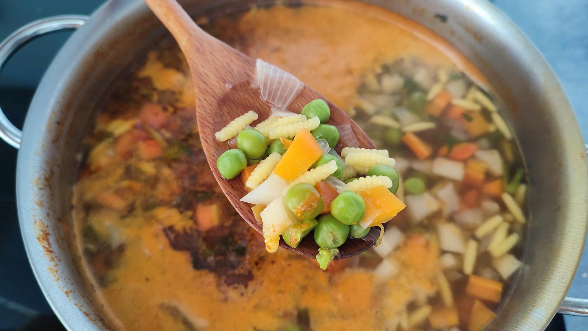 Close-up of a wooden spoon holding fresh vegetables over simmering soup. - easy vegan recipes