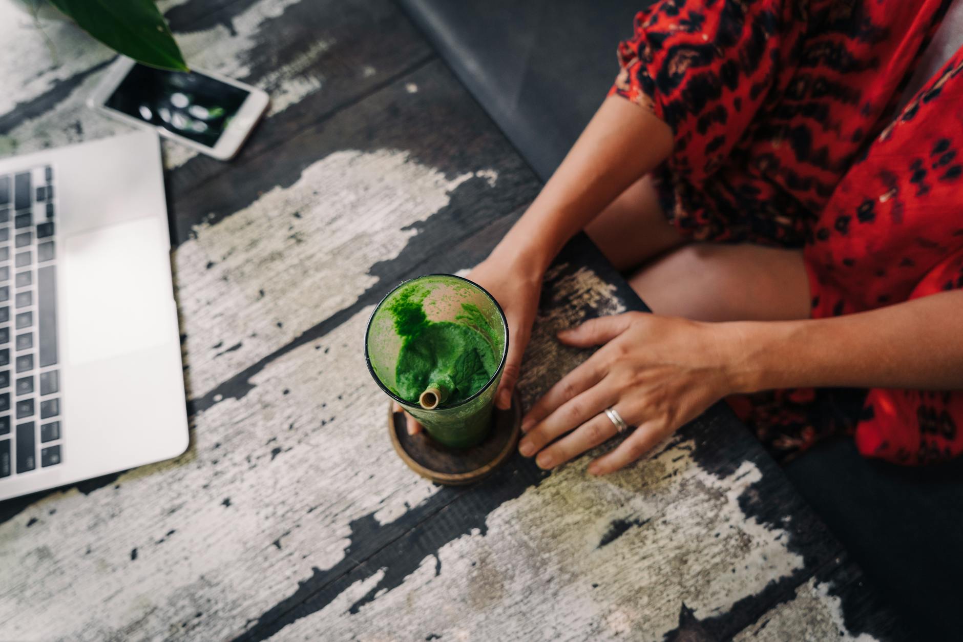 A vibrant green smoothie next to a laptop and phone on a rustic table, perfect for a healthy lifestyle setting. - green smoothie benefits