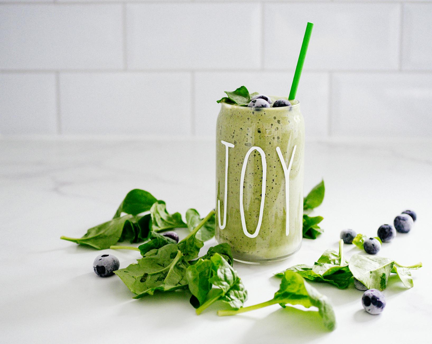 Refreshing green smoothie with spinach and blueberries in a glass labeled 'JOY' on a white background. - healthy smoothie recipes