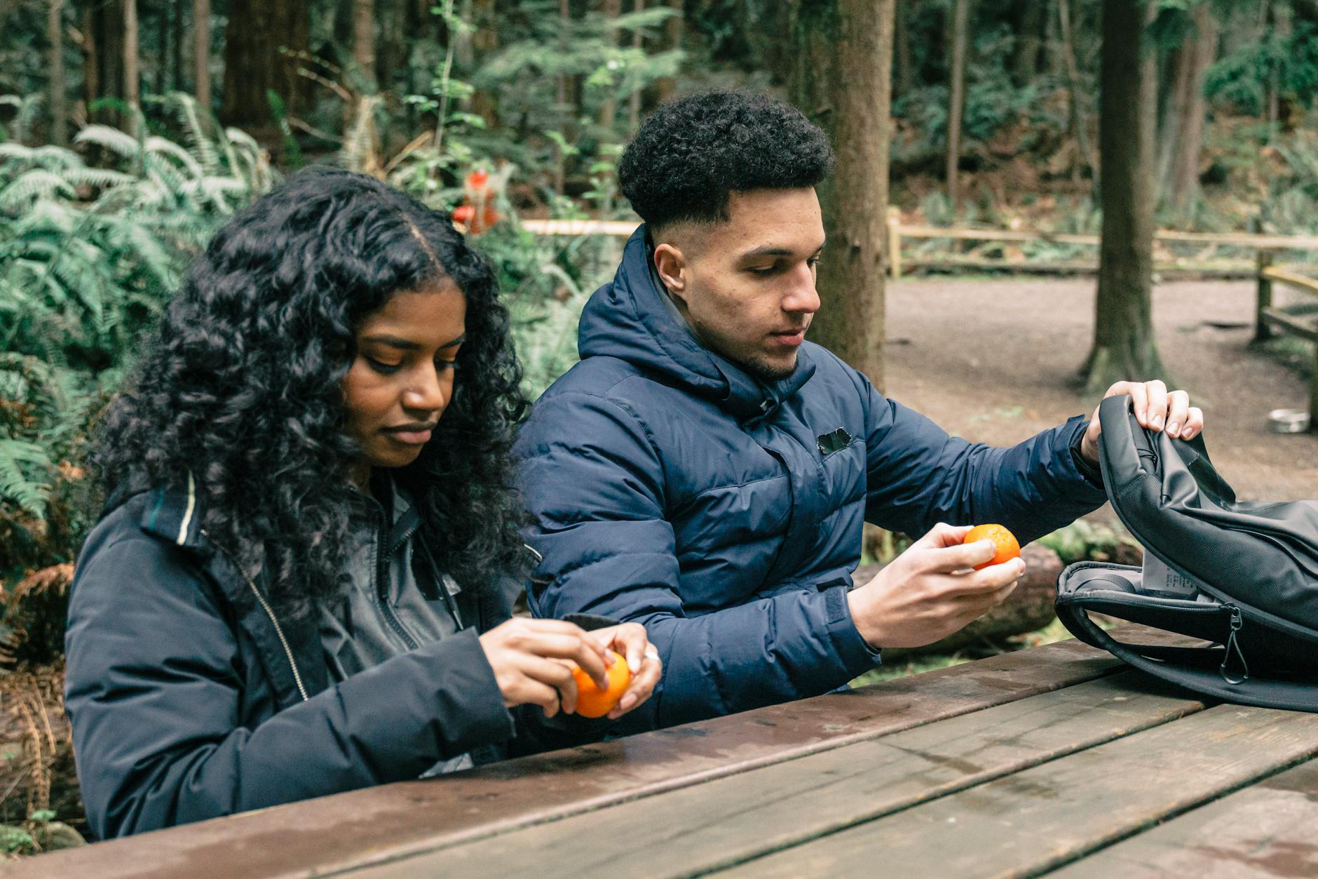 Friends enjoying a snack with oranges at a picnic table in a lush forest. - hiking energy snacks