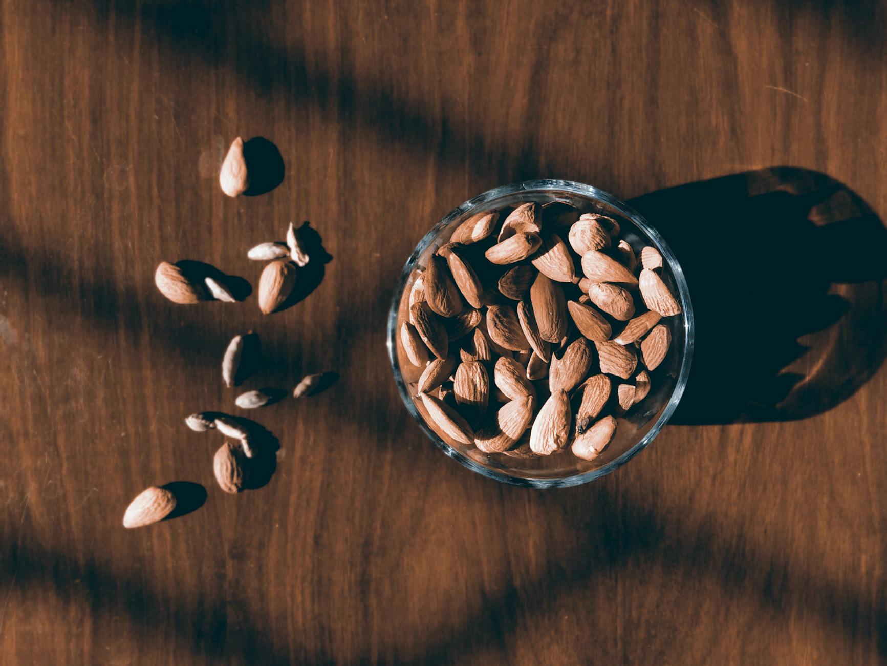 Close-up of almonds in a glass bowl on a wooden surface with dramatic shadows. - hiking energy snacks