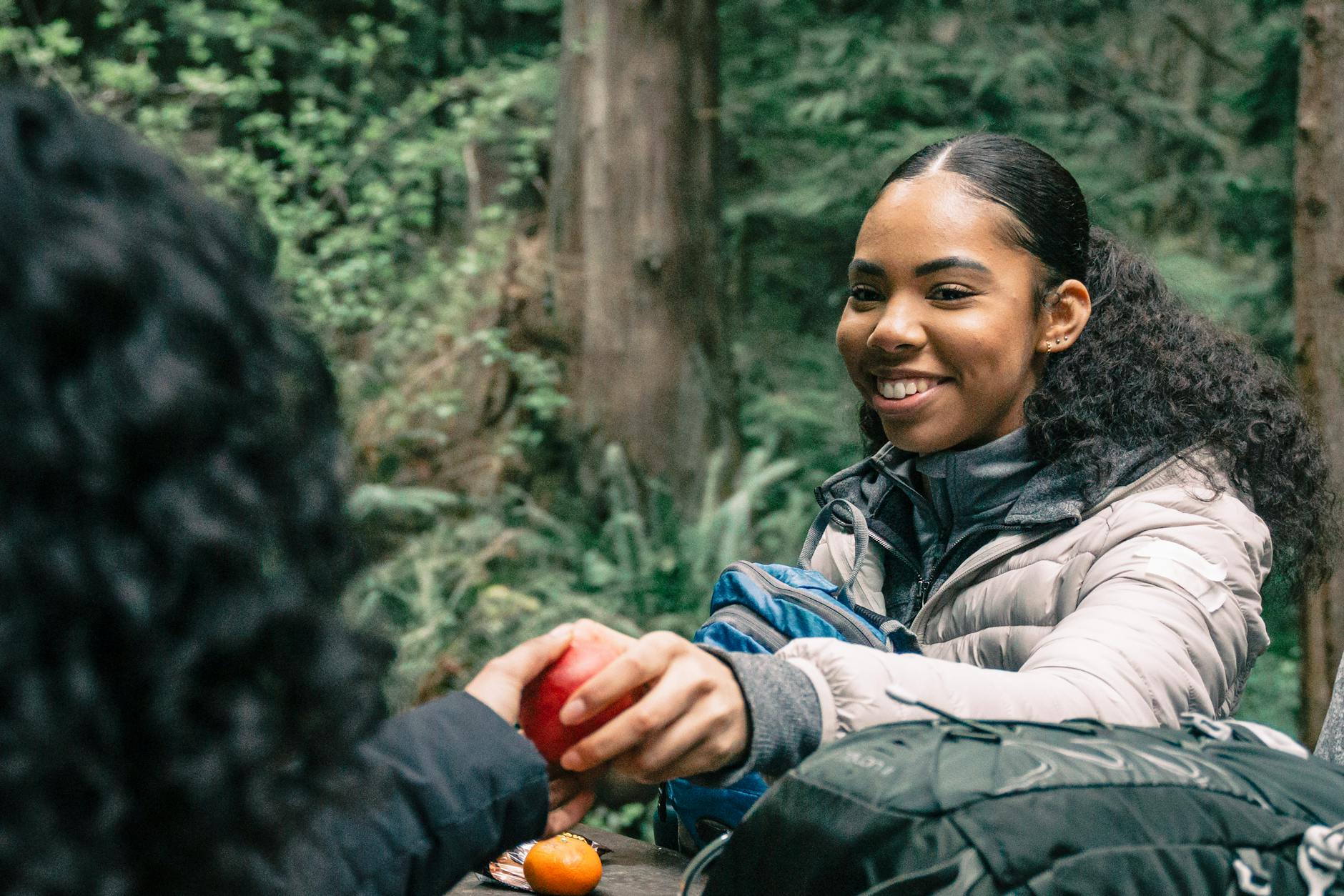 Woman in hiking gear shares an apple with a friend during a forest hike, showcasing joy and companionship. - hiking trail snacks