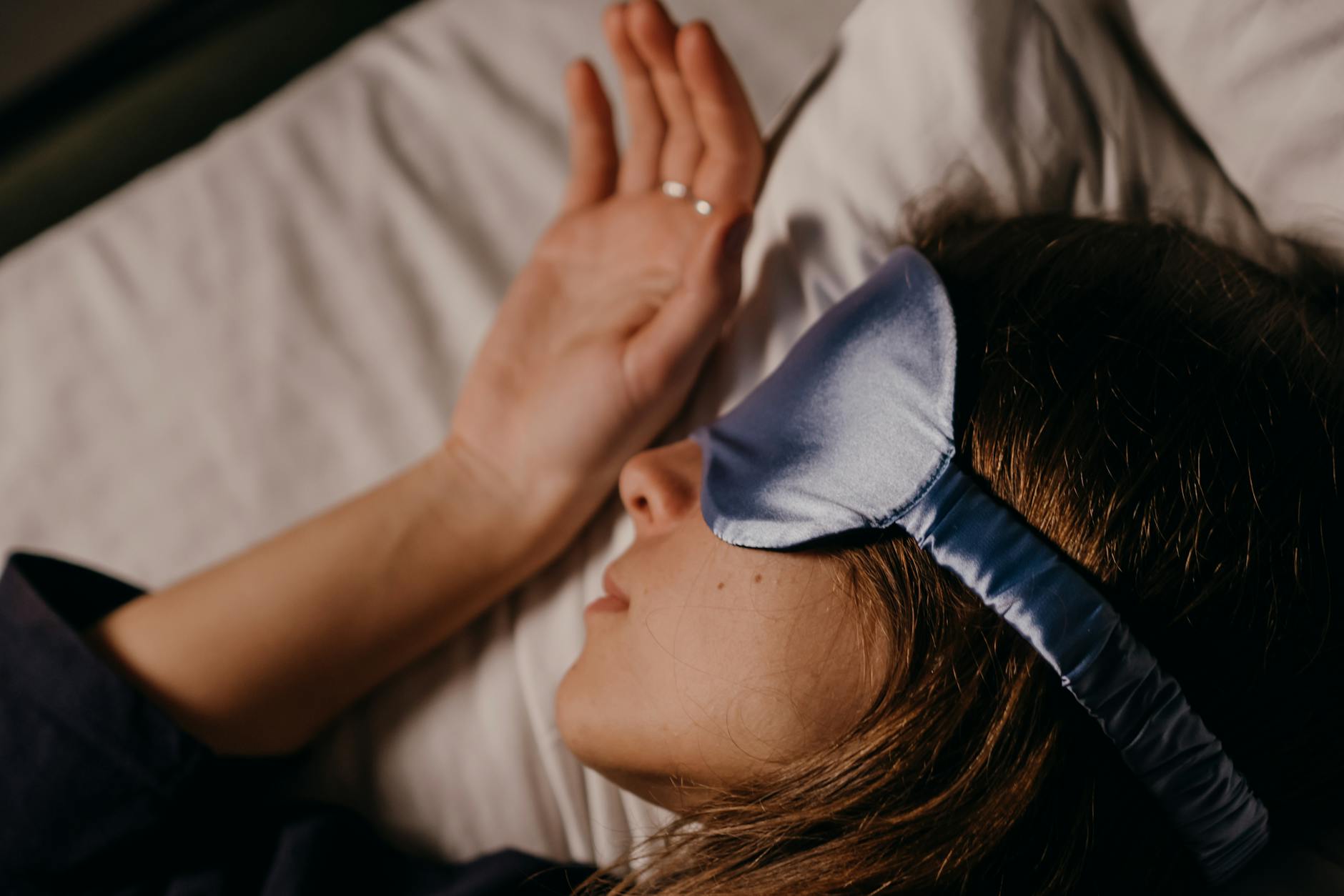 A woman peacefully sleeping in bed, wearing a blue silk eye mask for comfort and relaxation. - magnesium for sleep