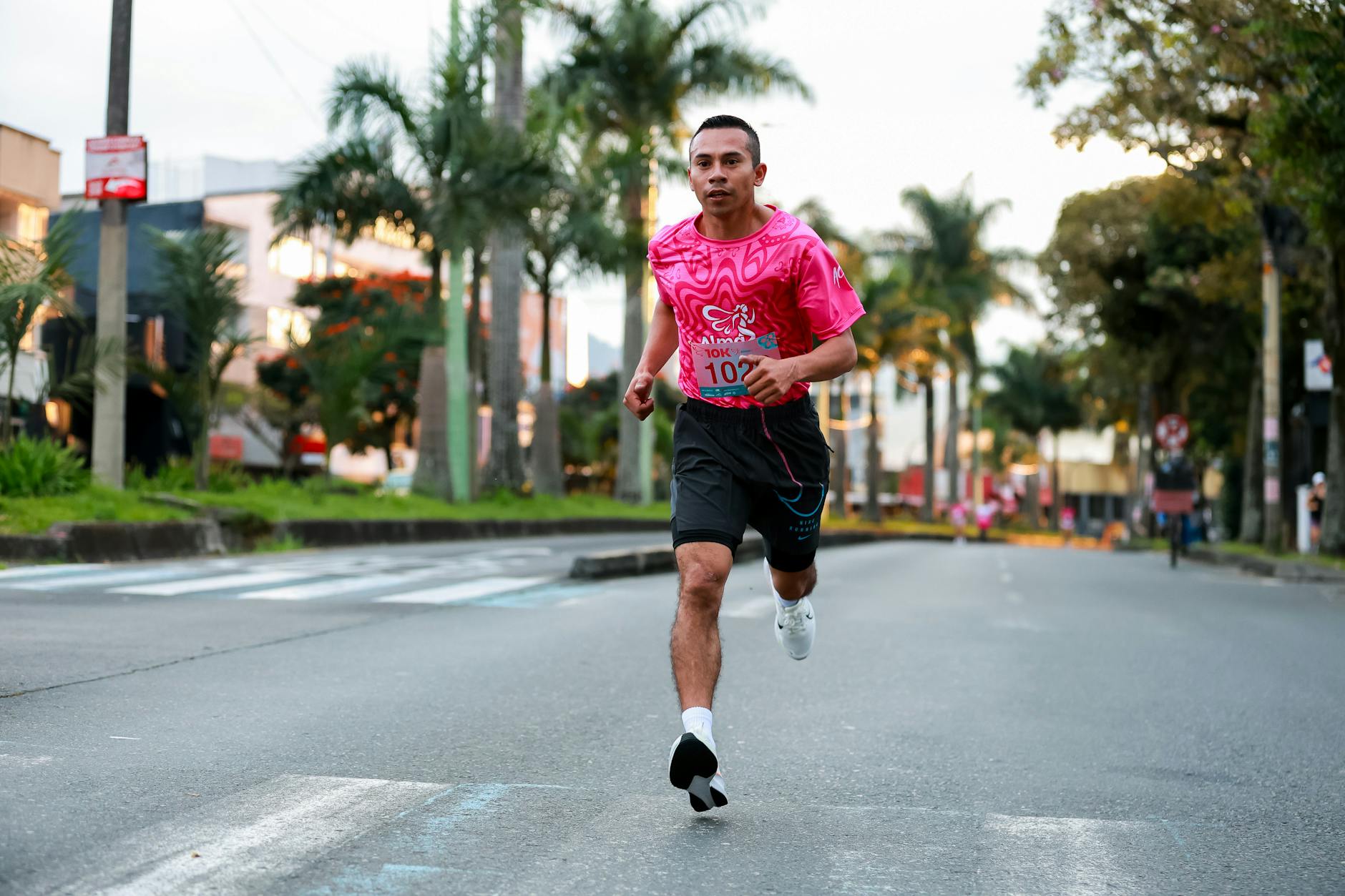 Energetic young man in pink sportswear running in a city marathon. - marathon recovery nutrition