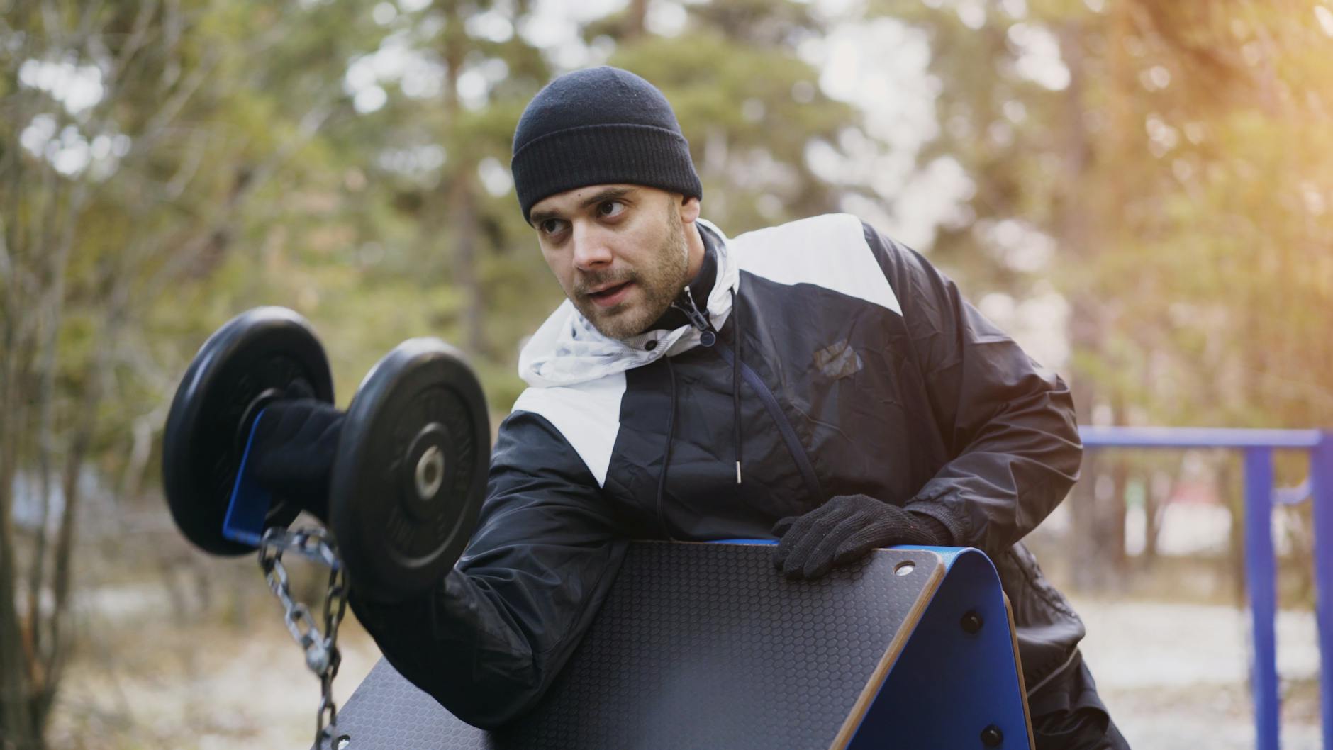 Man exercising with dumbbells outdoors in winter gear. - outdoor strength training