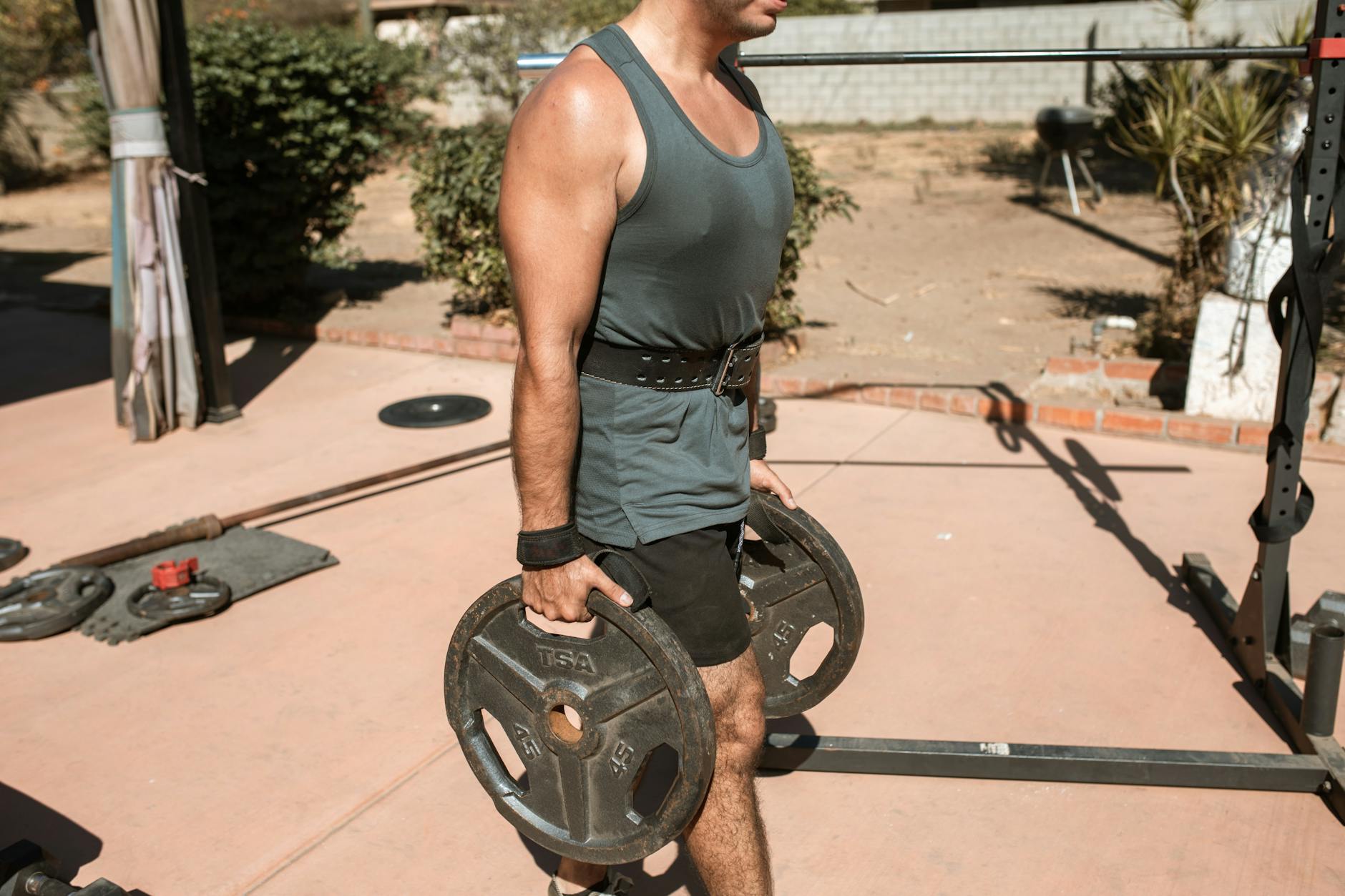 Man lifting heavy weights in an outdoor gym setting under bright sunlight. - outdoor strength training