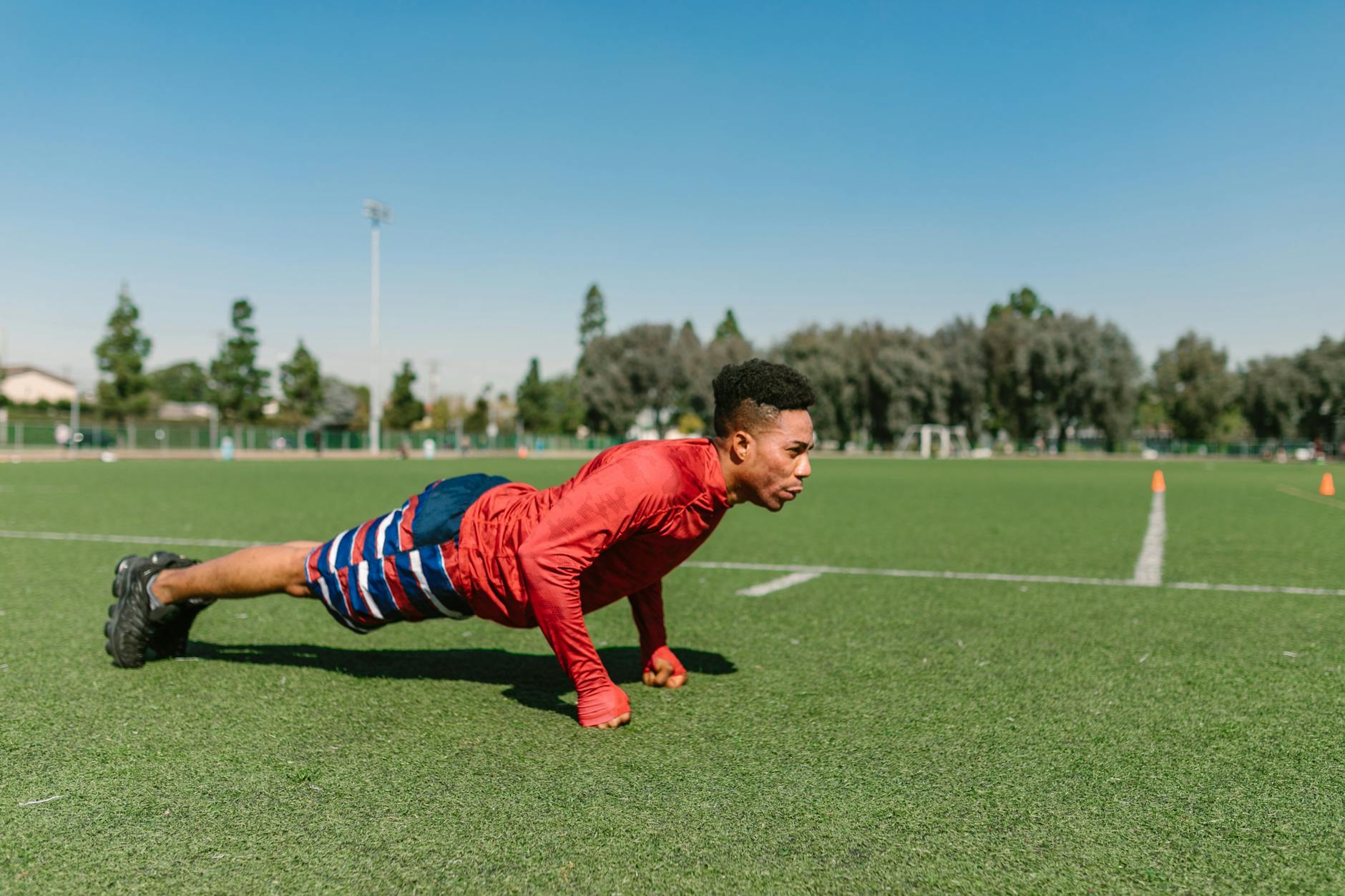African American man performs push-ups on a sunny soccer field during a workout session. - plyometric exercises
