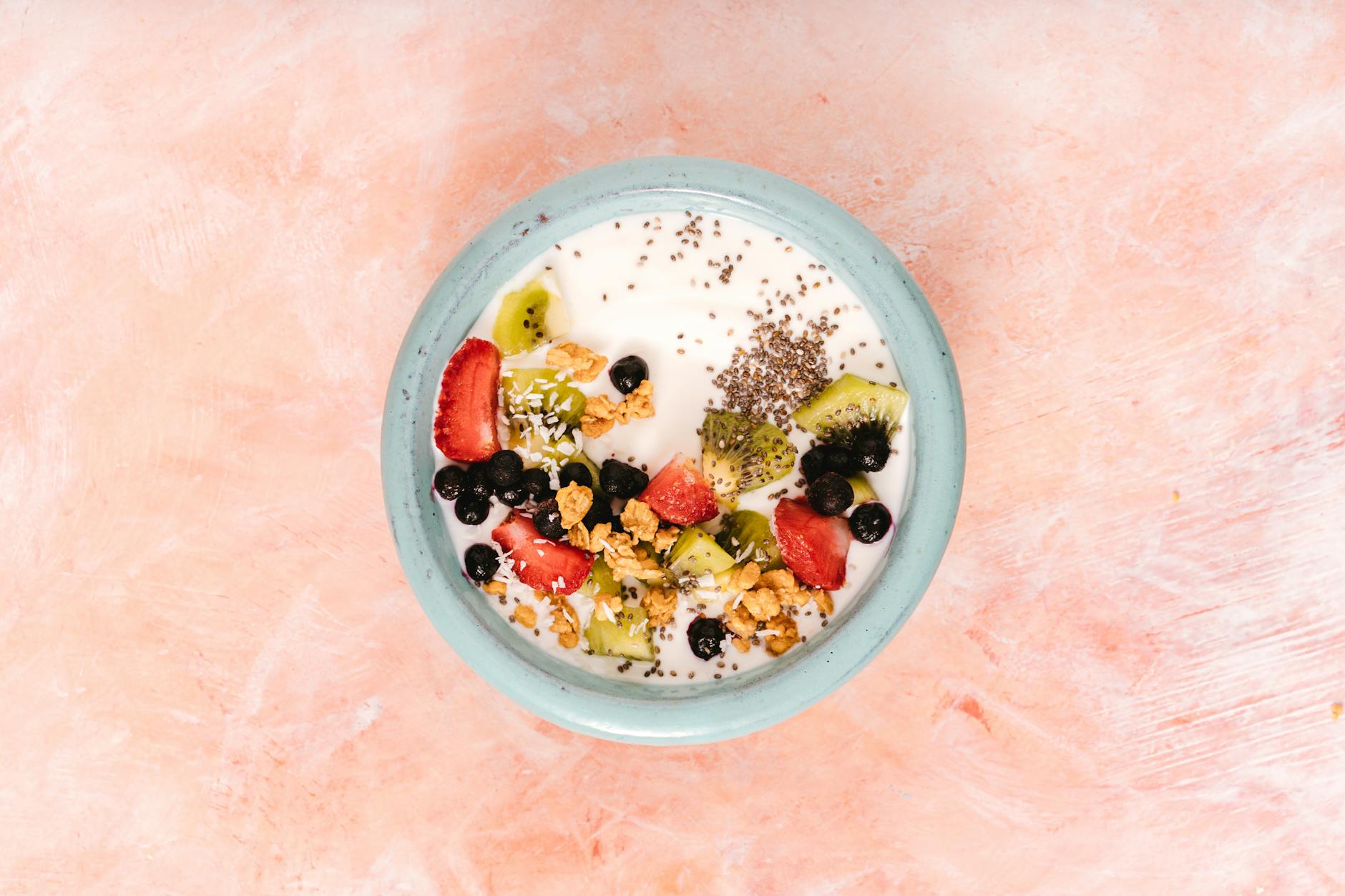 Top view of a nutritious breakfast bowl with yogurt, fresh fruits, and seeds on a pink background. - probiotic recipes gut health