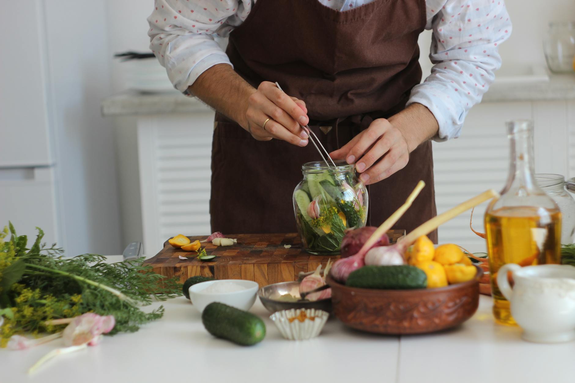 Close-up of a person pickling vegetables with tweezers in a jar, showcasing fresh ingredients on a kitchen table. - probiotics gut health