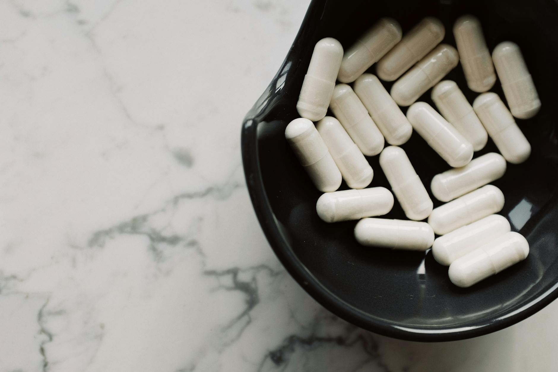 Close-up of white capsules in a black bowl on a marble surface, symbolizing healthcare and medication. - probiotics gut health