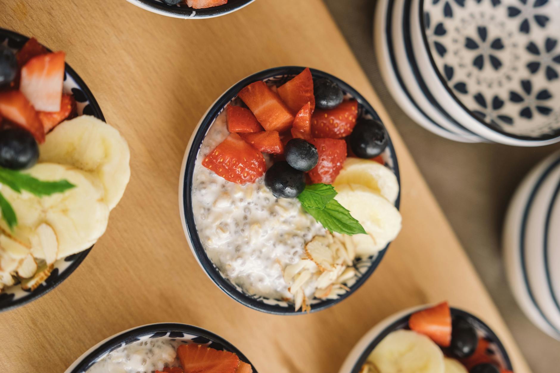 Overhead view of oatmeal bowls topped with fresh fruits like bananas, strawberries, and blueberries. - spring energy breakfast