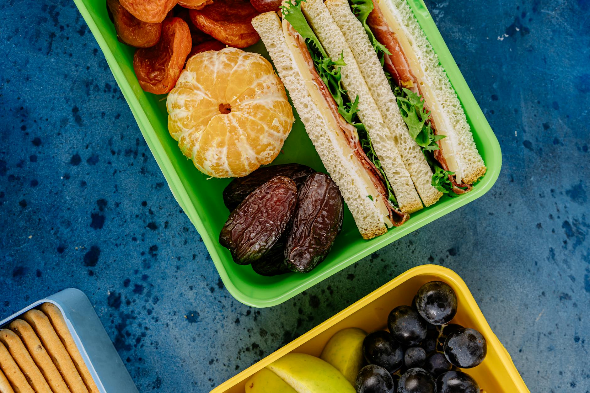 Top view of colorful lunch boxes filled with healthy sandwiches, fruits, and snacks. - spring energy lunch