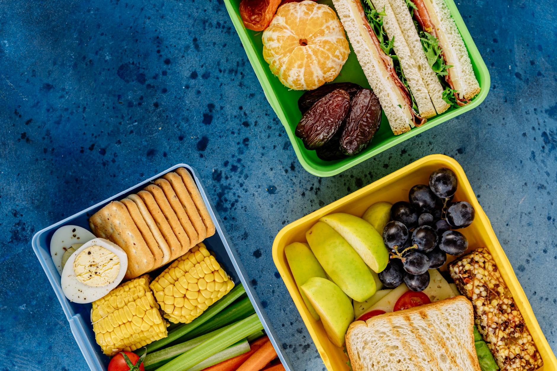 Top view of diverse and healthy lunchbox meals including fruits, veggies, and sandwiches. - spring energy lunch