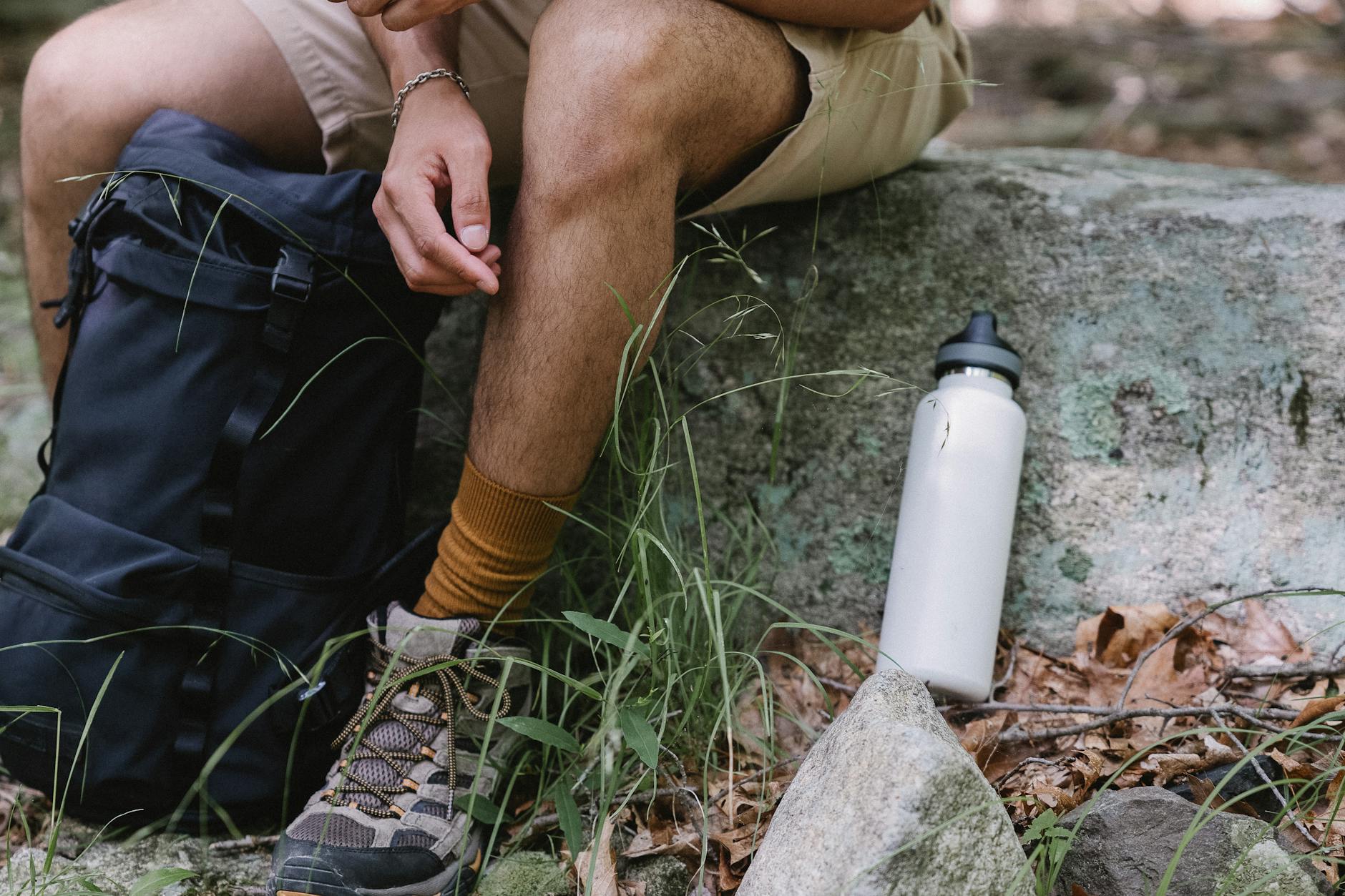 Close-up of a hiker with gear, resting on a stone outdoors. - spring hike hydration