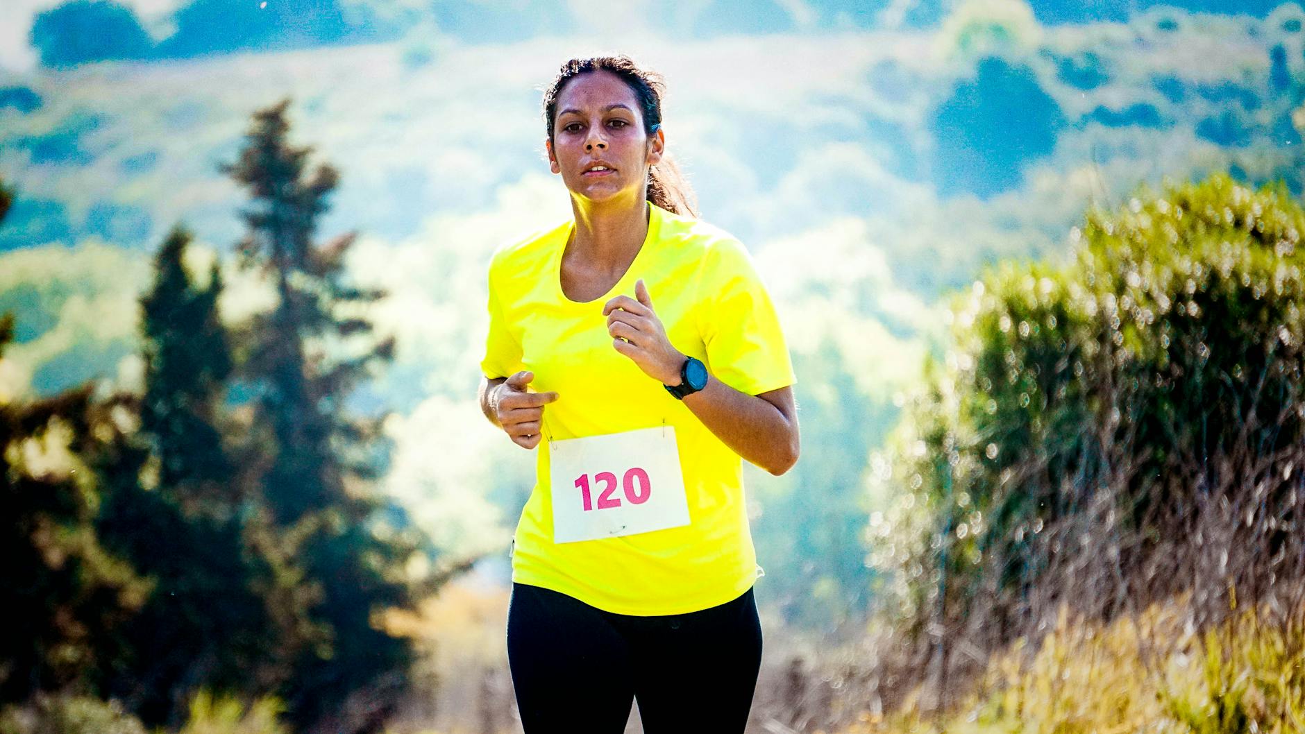 A fit woman running a marathon in a vibrant outdoor landscape, wearing a bright yellow shirt. - spring running trails
