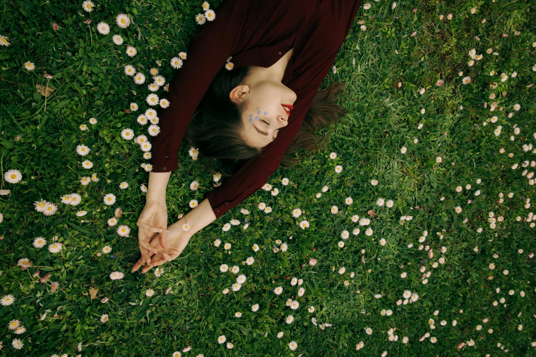 Top view of a woman relaxing in a lush flowered field, eyes closed. - spring self care