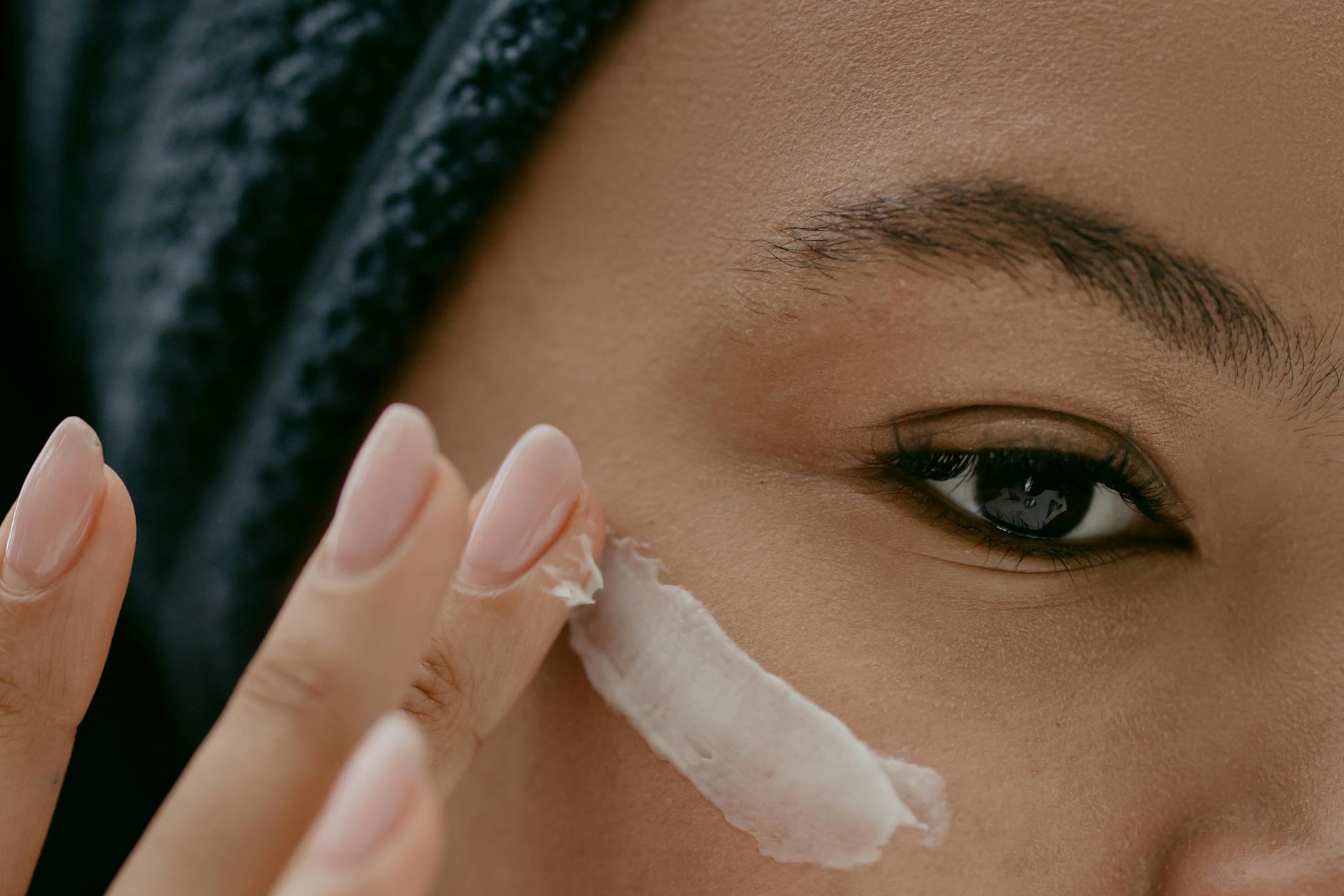 Extreme close-up of a woman applying cream to her cheek for healthy skin care. - spring skin glow