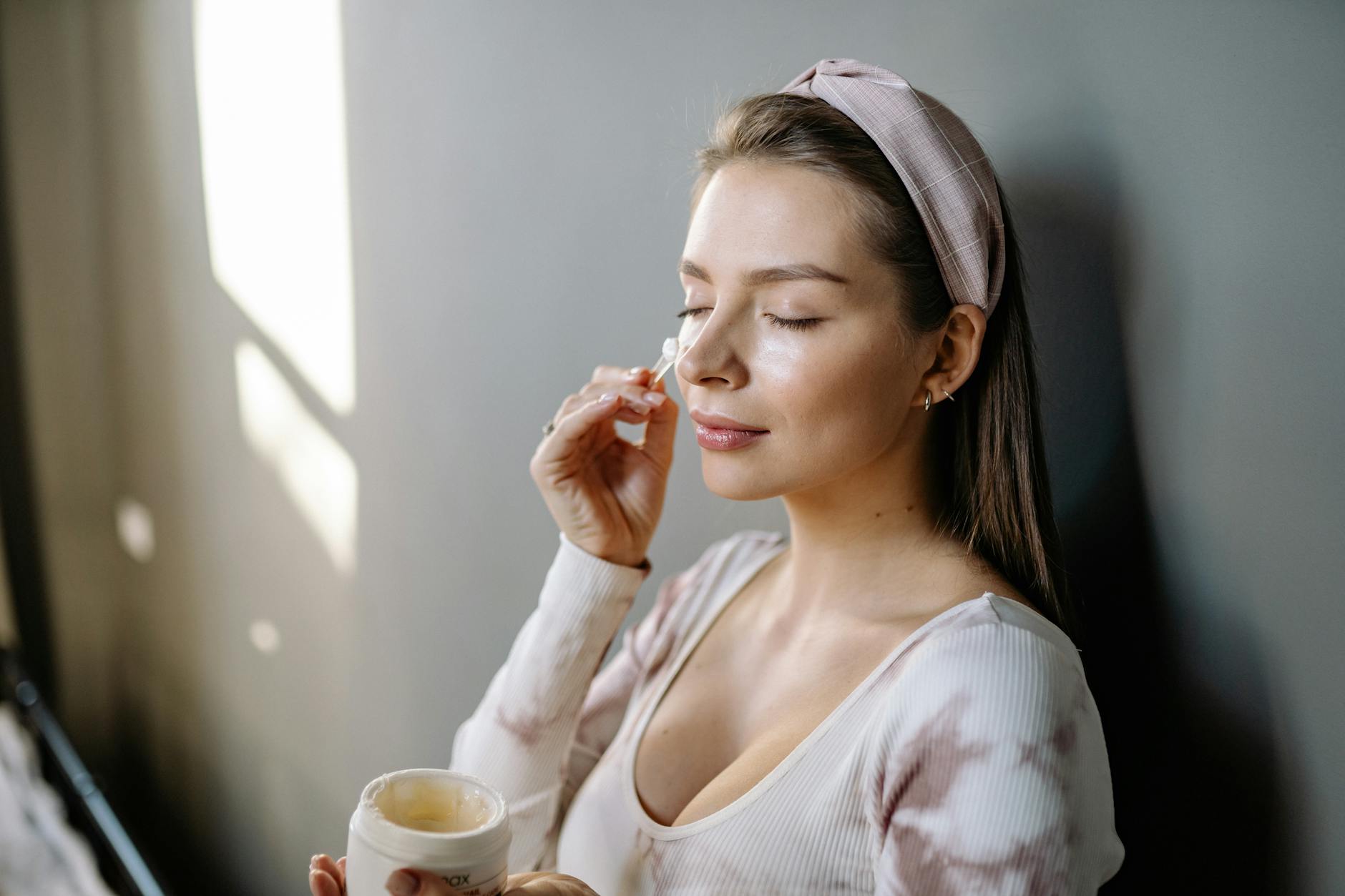 A woman with eyes closed applying skincare cream to her face, emphasizing self-care. - spring skincare tips
