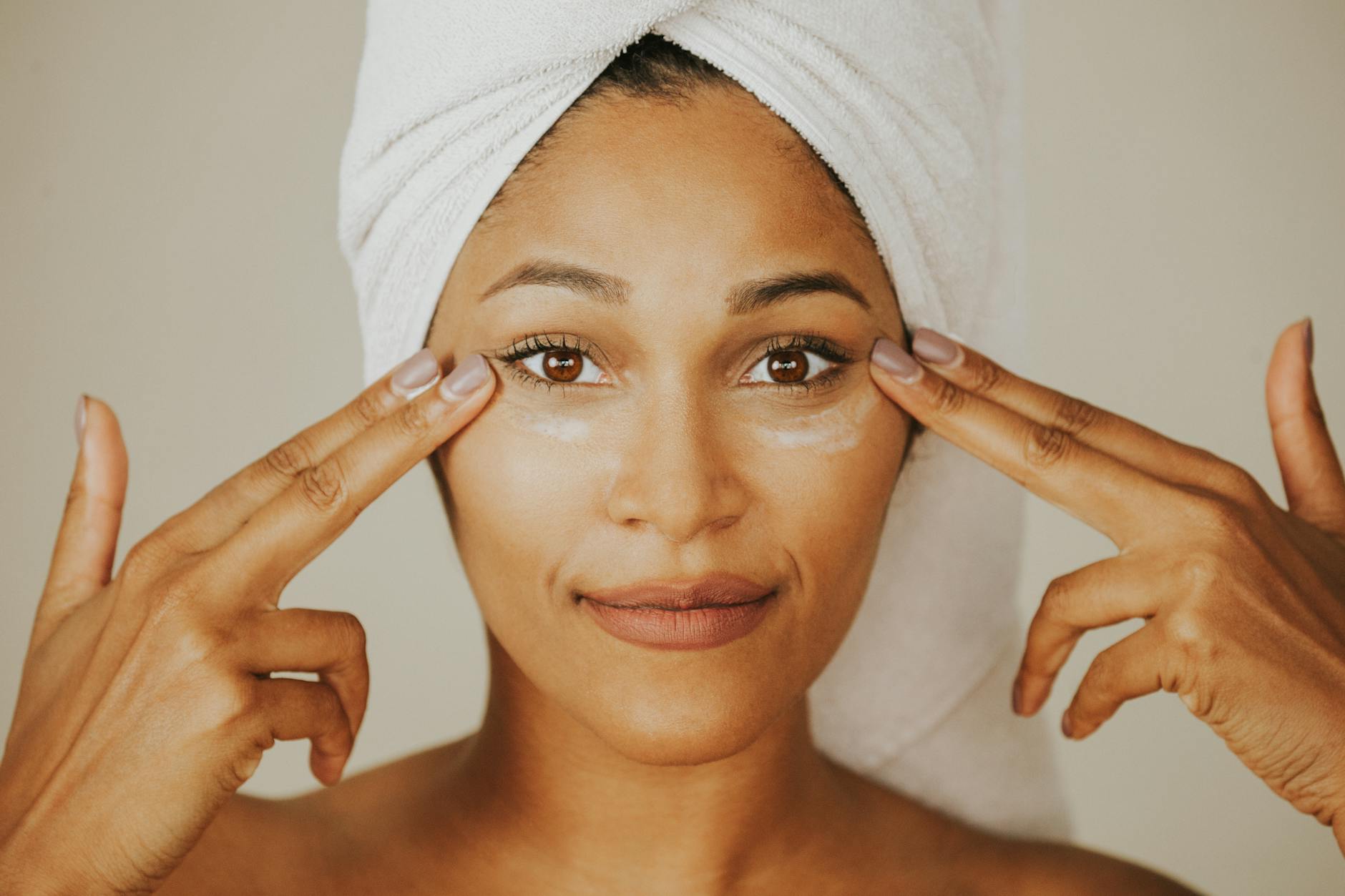 Woman applying facial cream with a towel wrapped on her head, highlighting skincare routine. - spring skincare tips